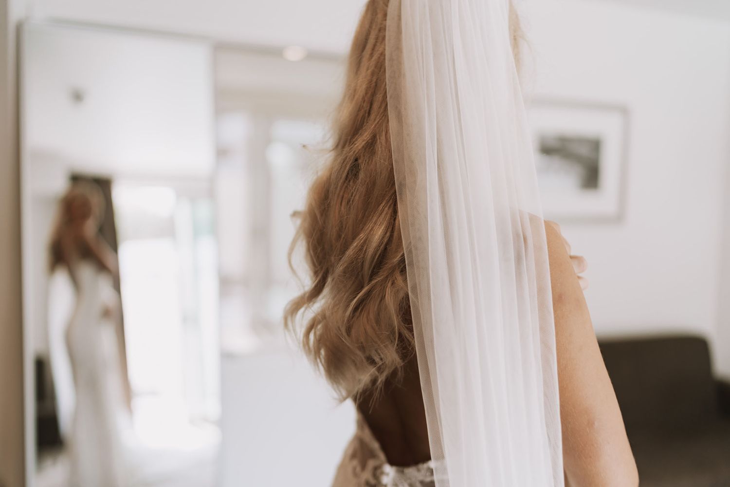 A long white veil flows beside wavy brown hair in a bright interior setting.
