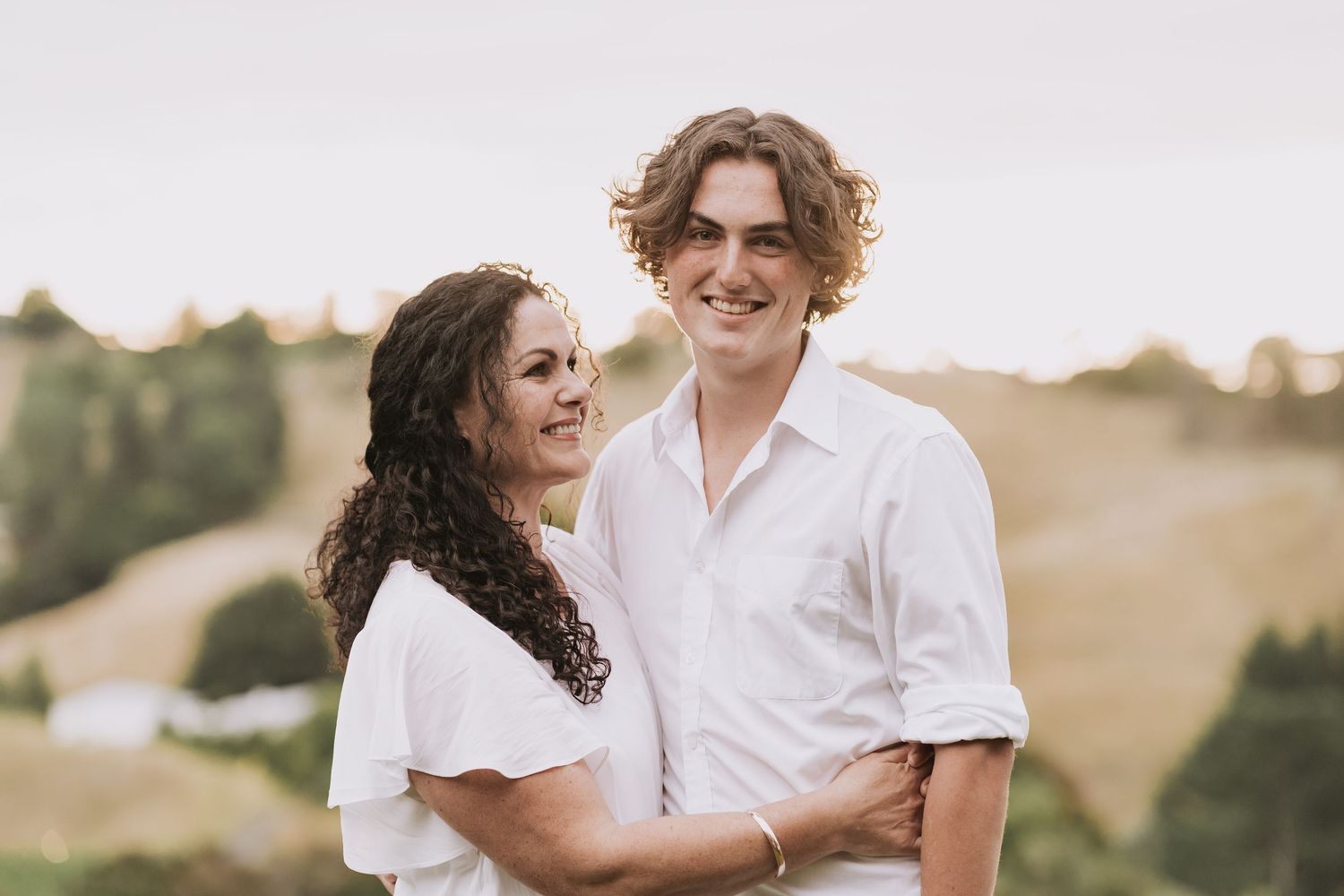 A couple in white outfits sharing a tender moment together outdoors against rolling hills during golden hour.