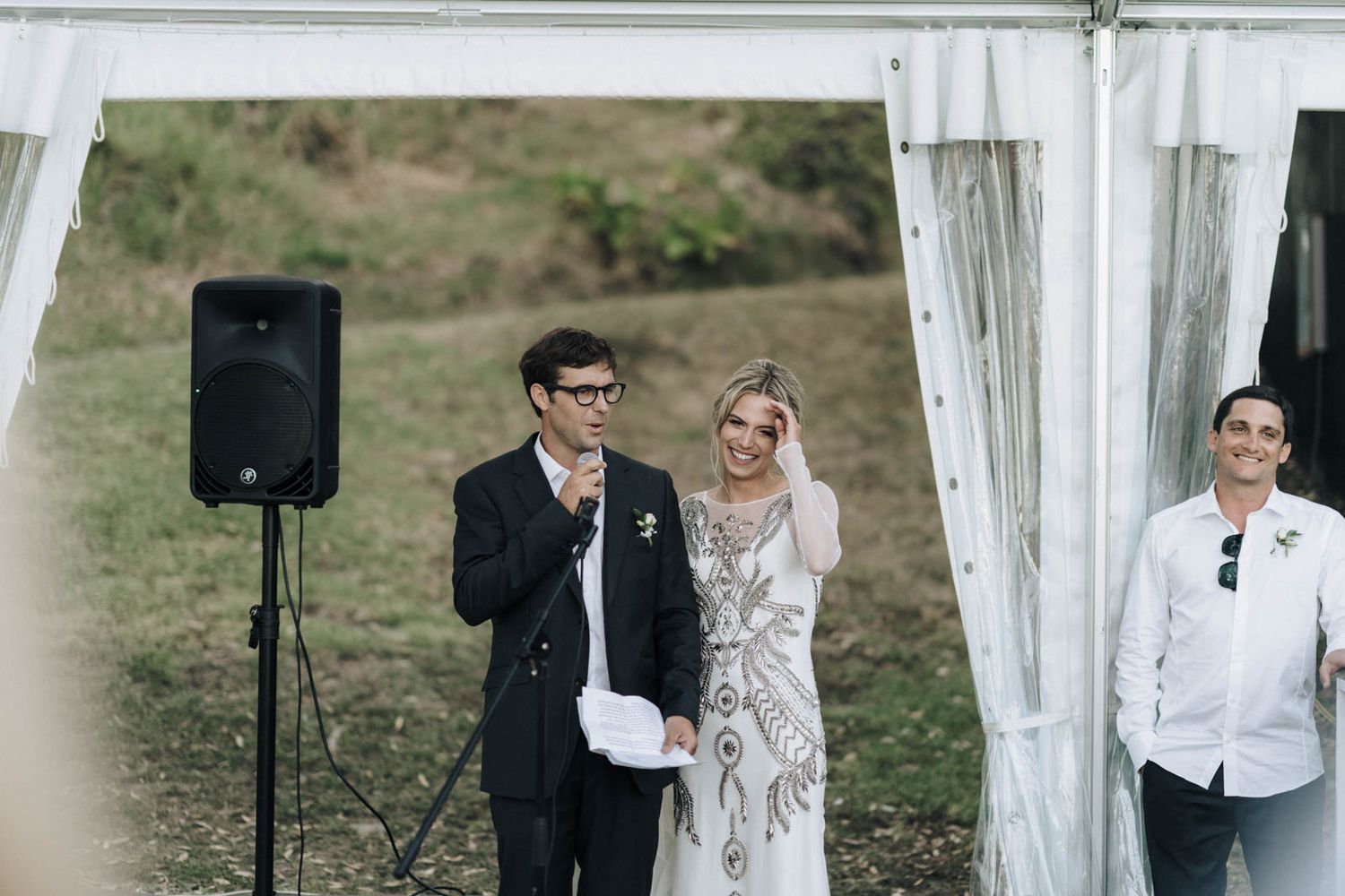 An outdoor wedding ceremony setup with white curtains and a speaker stand in a natural setting.