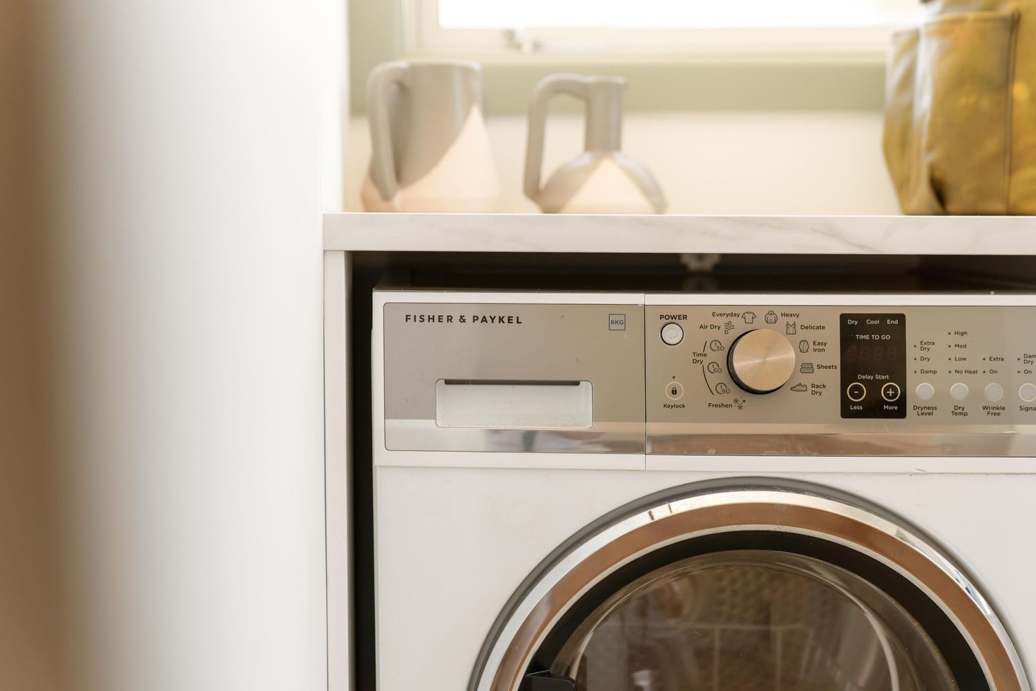 Row of white front-loading washing machines and dryers in a clean laundry facility.