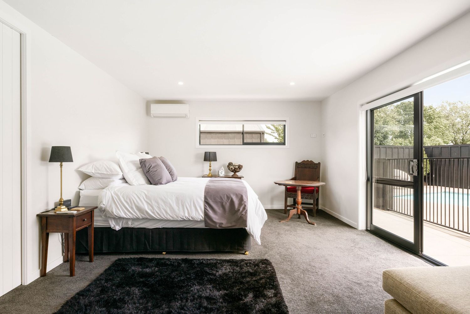 Modern bedroom with white walls and decor featuring a sliding glass door, black rug, and minimalist furniture.