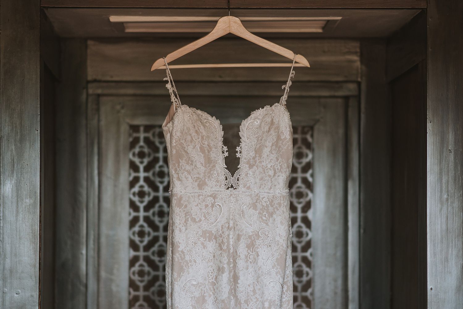 Wooden hangers lined up neatly on a chrome rod against a decorative lattice wall pattern in muted tones.
