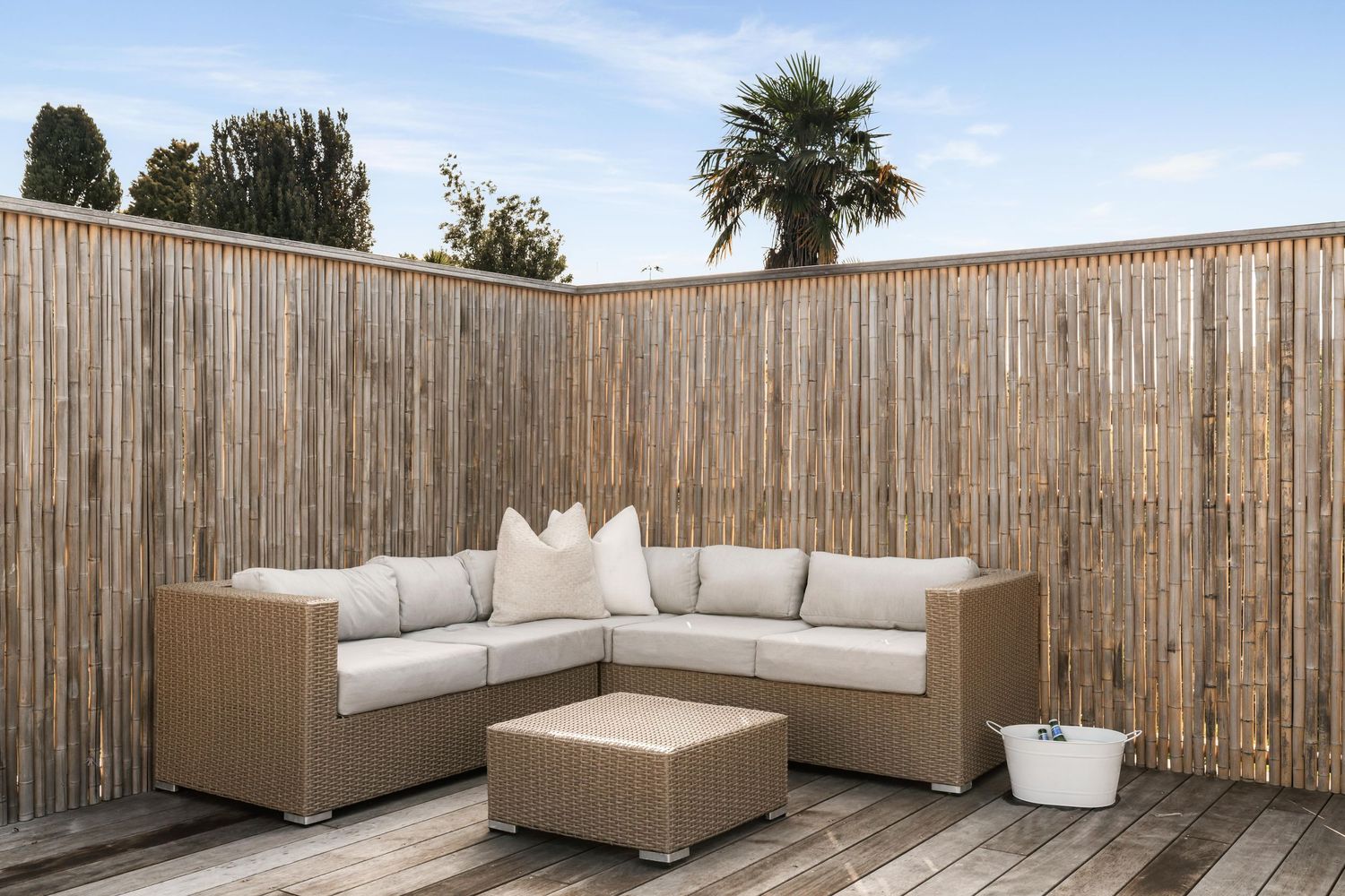 Outdoor lounge area with beige sectional sofa against bamboo privacy fence.