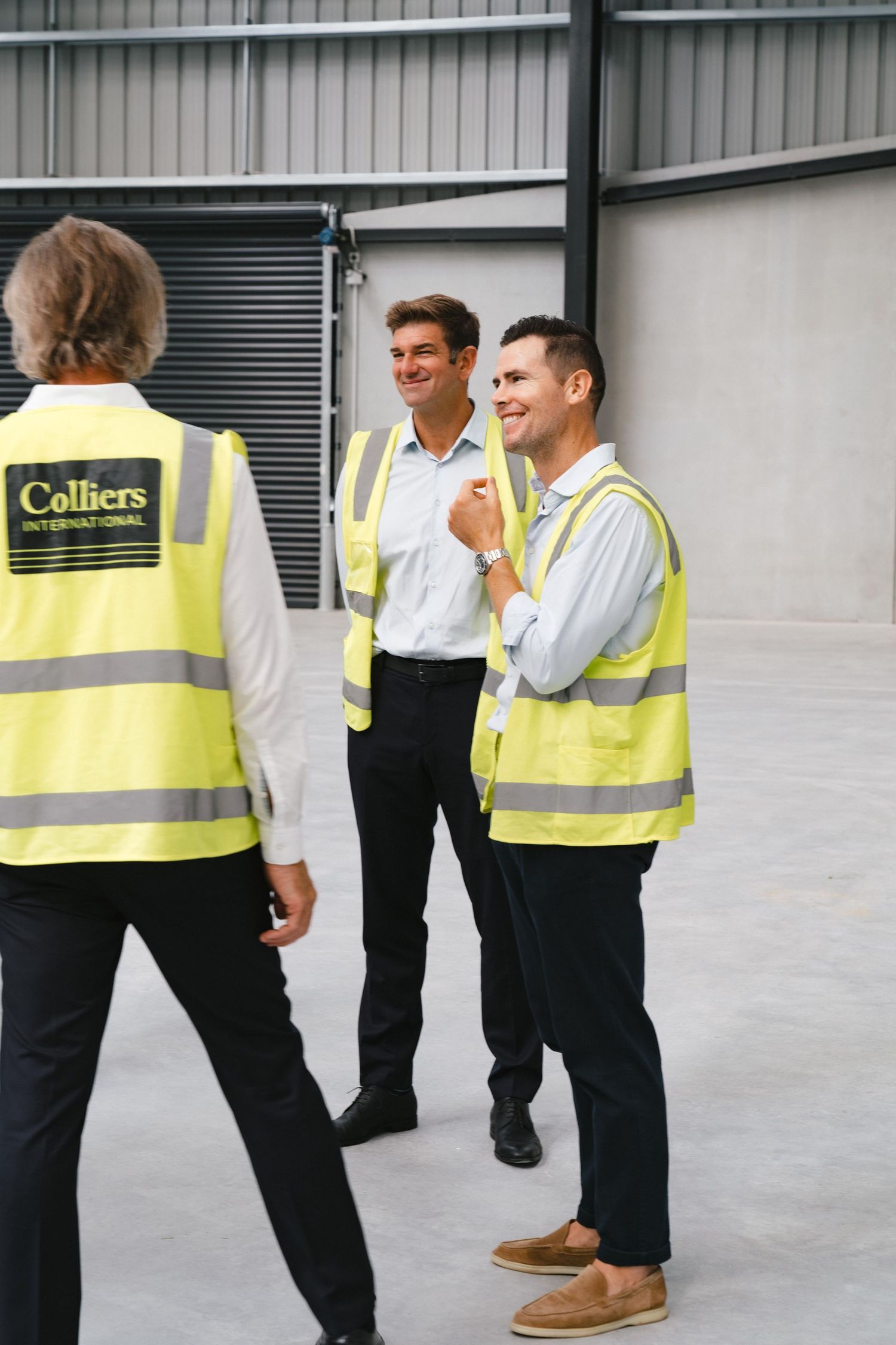Group wearing high-visibility vests inspecting an industrial warehouse space.