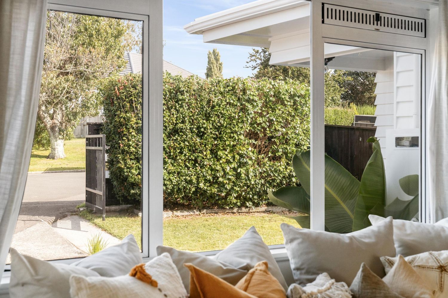 Cozy window seat with plush cushions overlooking garden with lush green hedge.