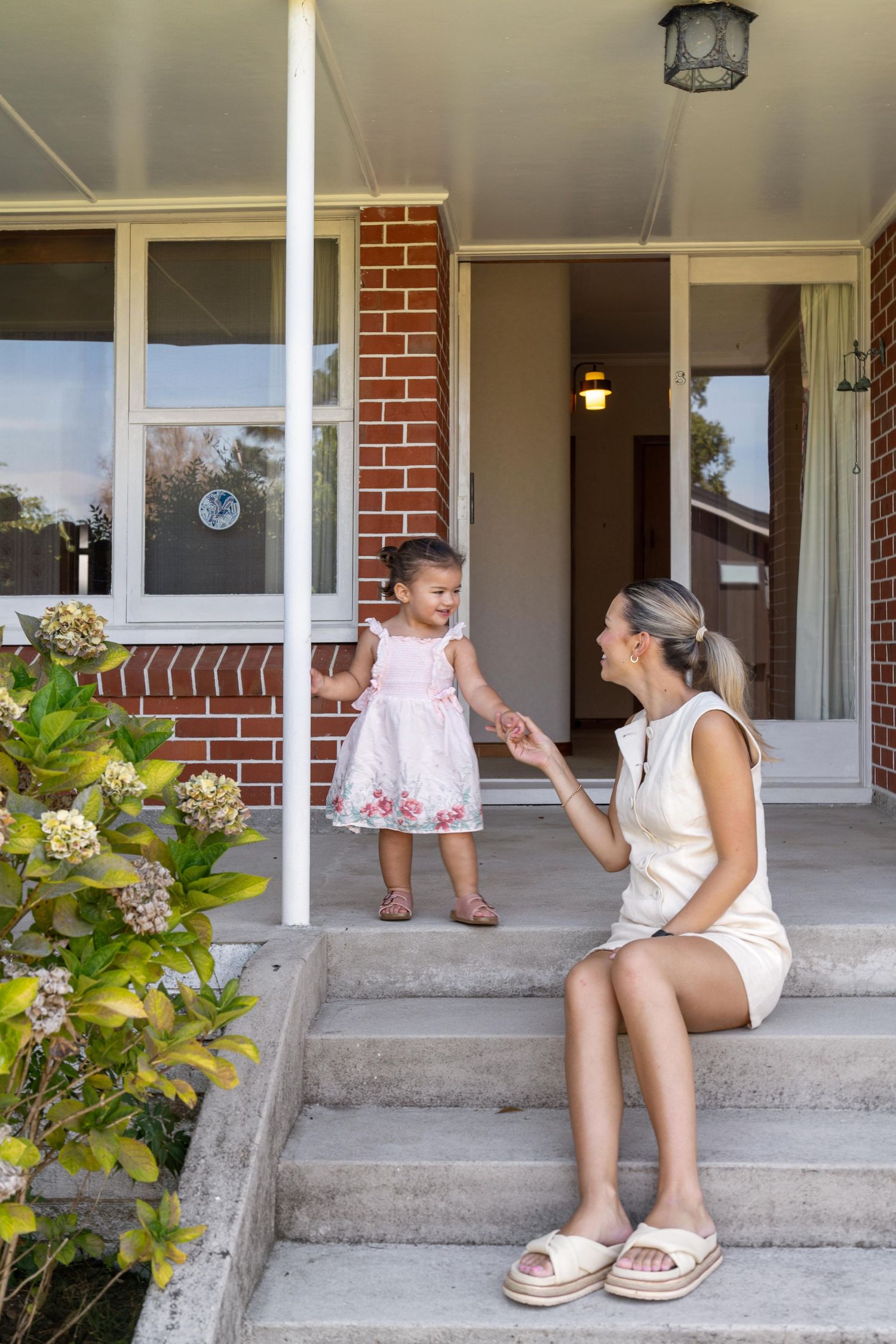 Sweet interaction on the front steps of a house with brick columns and green plants nearby.