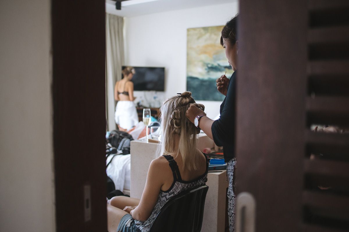 Person getting hair and makeup done in preparation for a wedding while others can be seen in background.