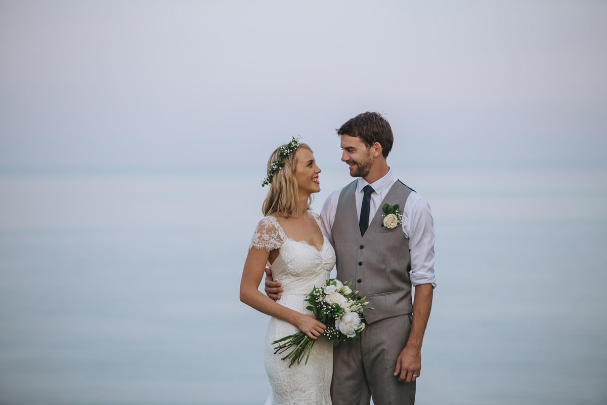 A romantic seaside wedding portrait with a misty ocean backdrop and lush white bouquet.