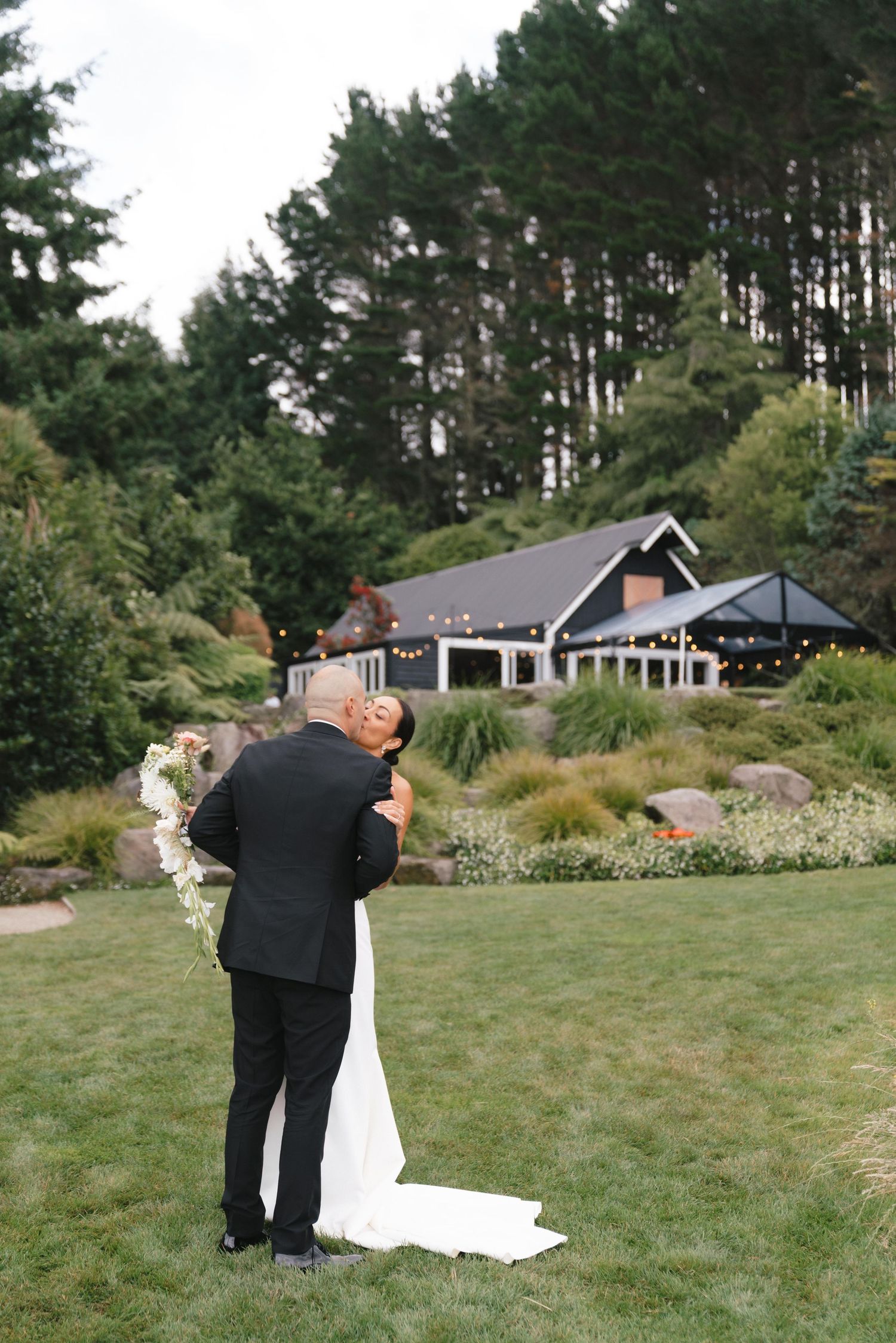 Wedding couple standing on a grassy lawn with pine trees in the background.