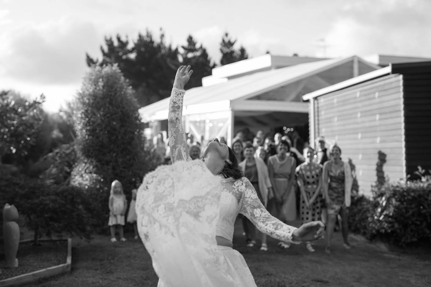 A delicate white wedding dress veil blows in the wind against a gray cloudy sky with trees in the background.