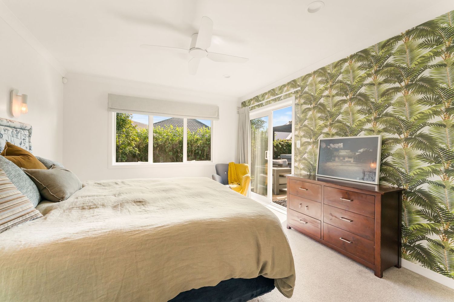 Modern bedroom with wooden furniture, white walls, and natural lighting through large windows.