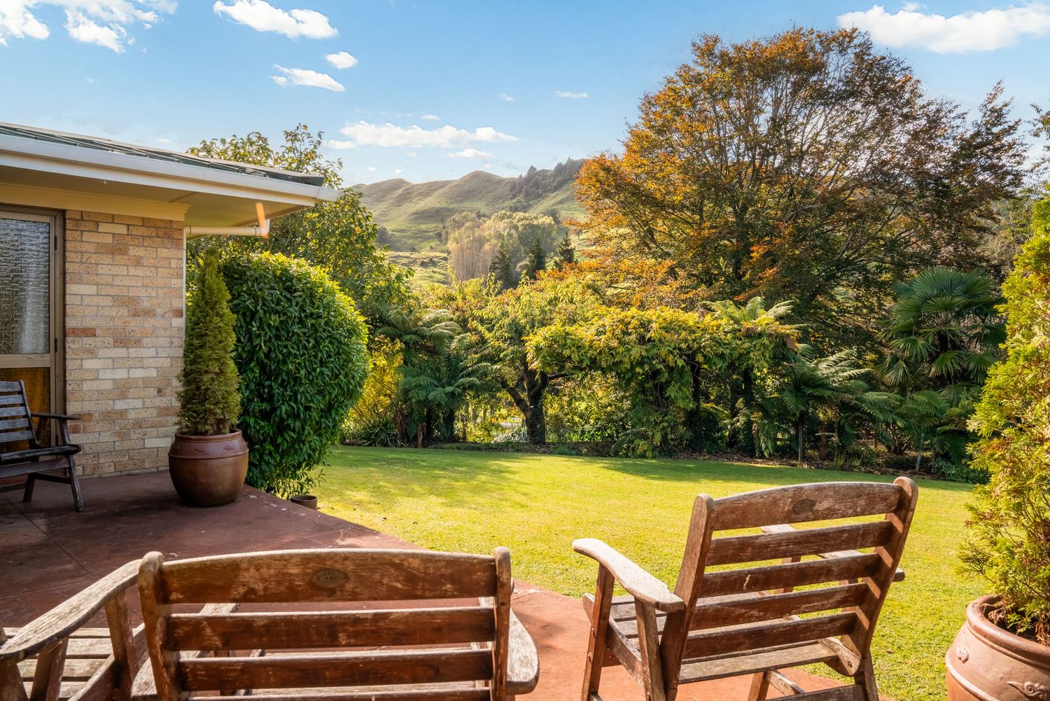 Wooden deck chairs on patio overlooking rolling green hills and mountain landscape.
