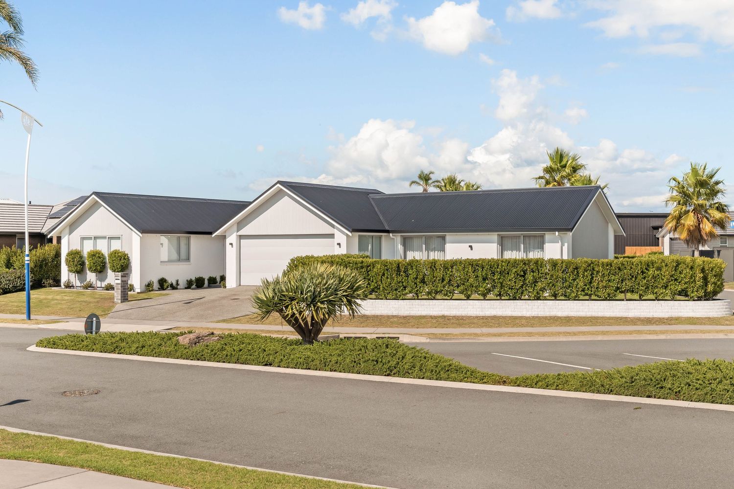 Modern single-story homes with white exteriors line a suburban street under a bright blue sky.