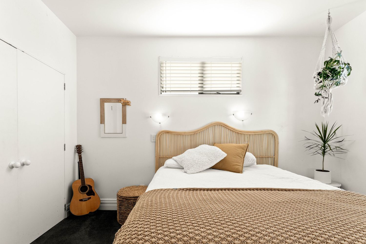 Minimalist white bedroom with wooden headboard and natural light from window.
