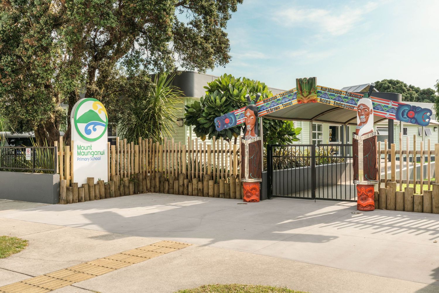 Street view of a gated community entrance with tropical landscaping and security features.