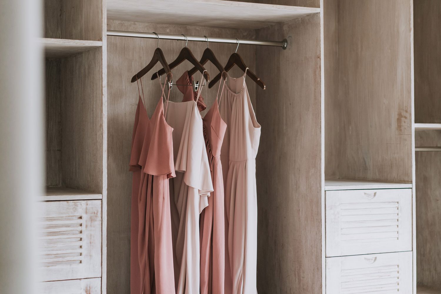 White minimalist closet system with built-in drawers and hanging rods displaying pink and white clothing items.