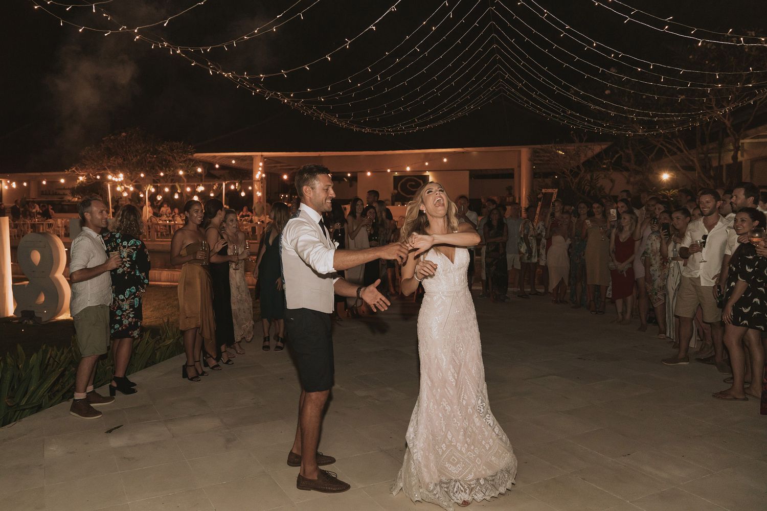 Couple shares their first dance under twinkling string lights at an outdoor evening wedding reception.