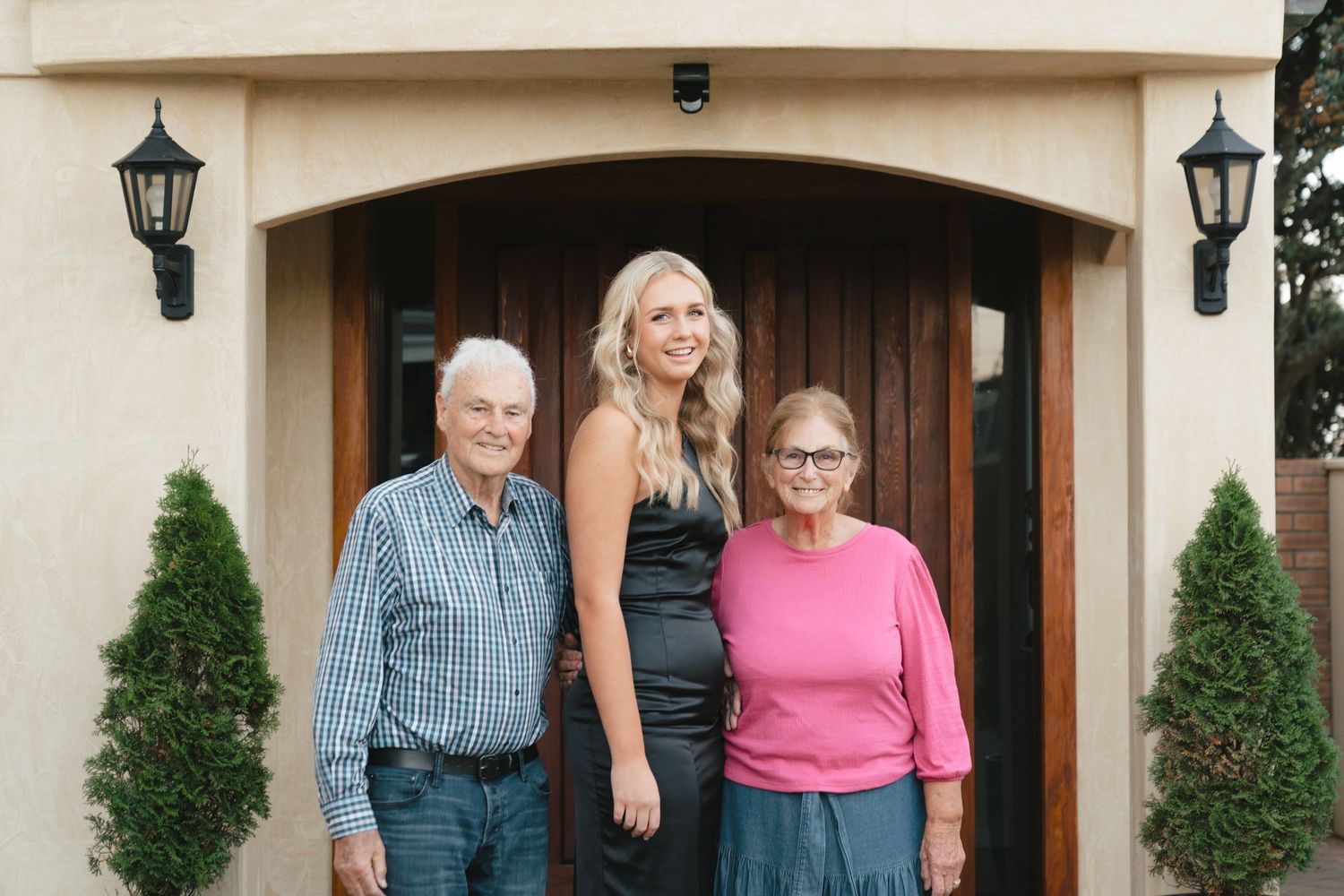 Three people stand together in front of elegant wooden door with decorative lanterns.