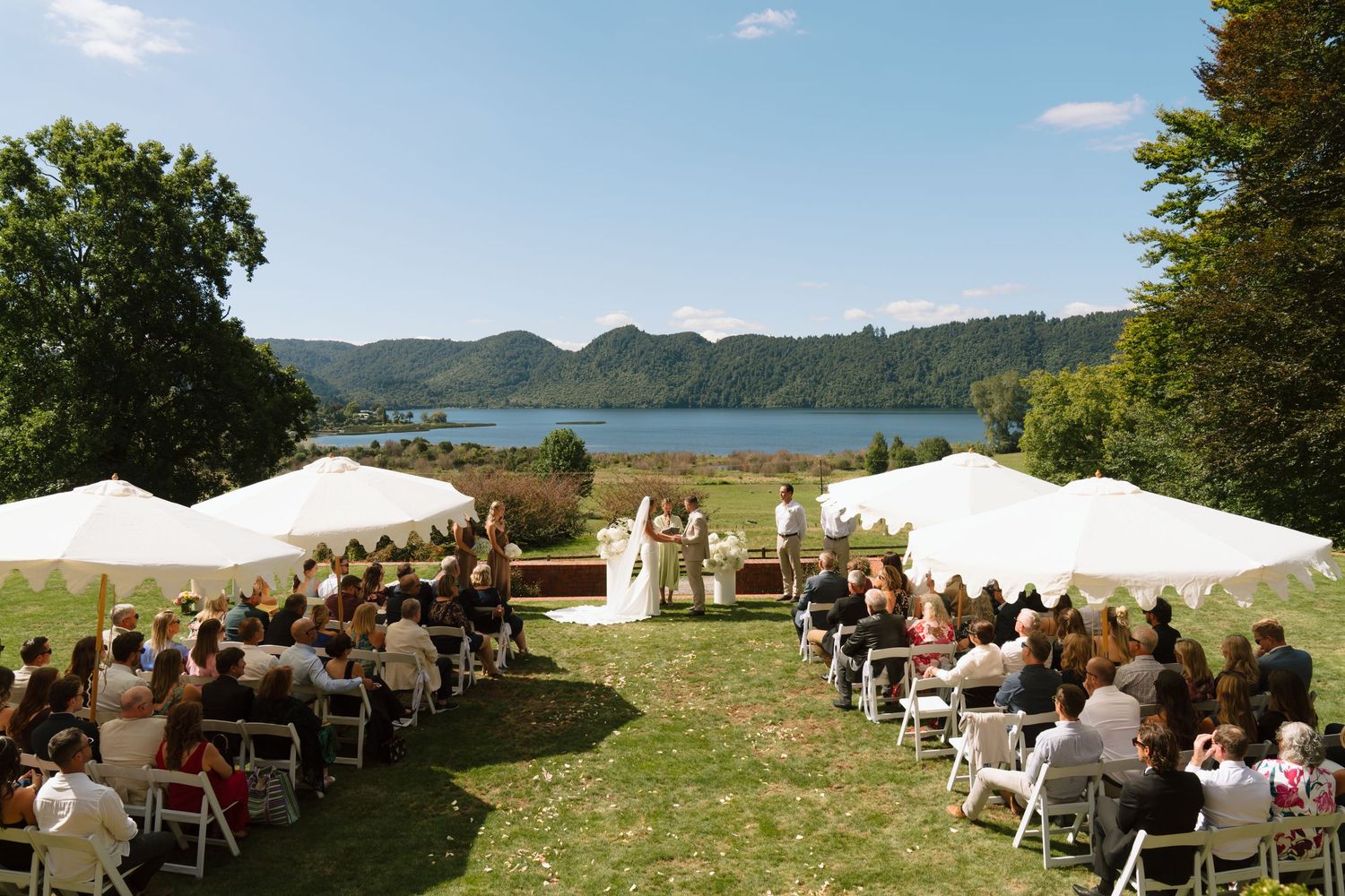 Outdoor wedding ceremony setup overlooking a scenic lake with white chairs arranged in rows on a grassy hillside.