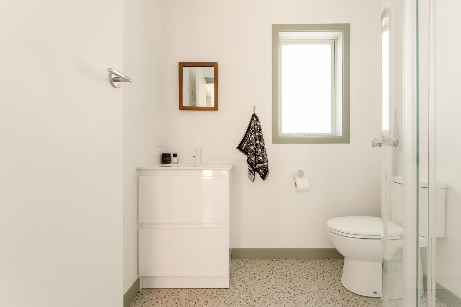 Clean white bathroom interior with modern fixtures and speckled tile flooring.