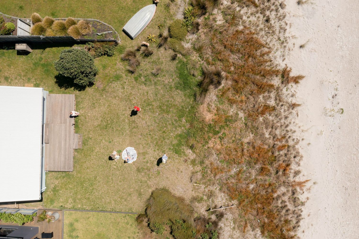 Aerial view of beachfront property with small structures and autumn foliage along sandy coastline.