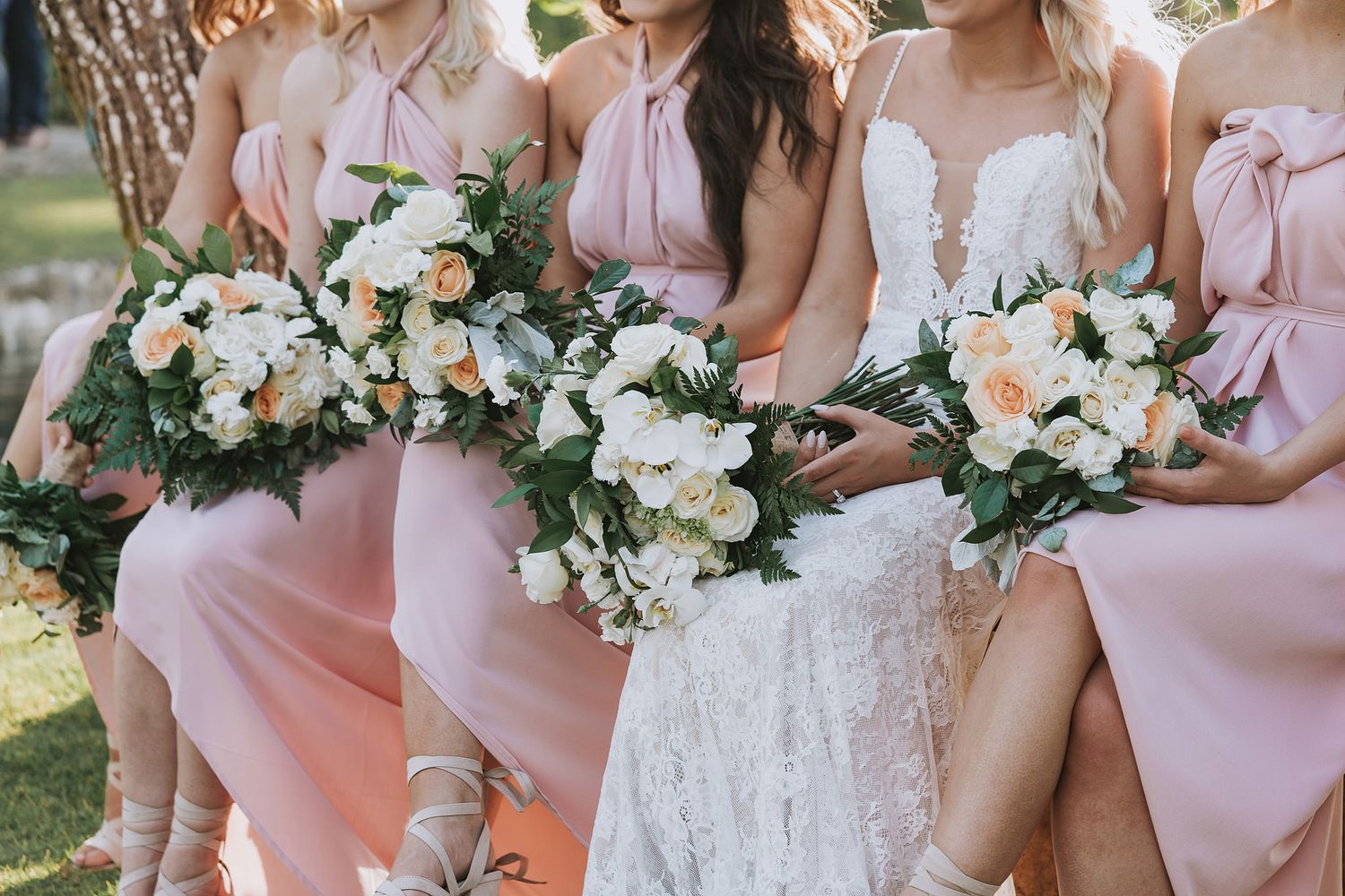 Wedding party in blush pink bridesmaid dresses holding elegant white and peach floral bouquets.