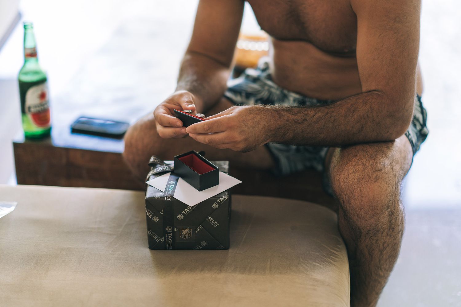 Close-up shot of someone sitting on a bed rolling cigarettes with a beer bottle on the table.