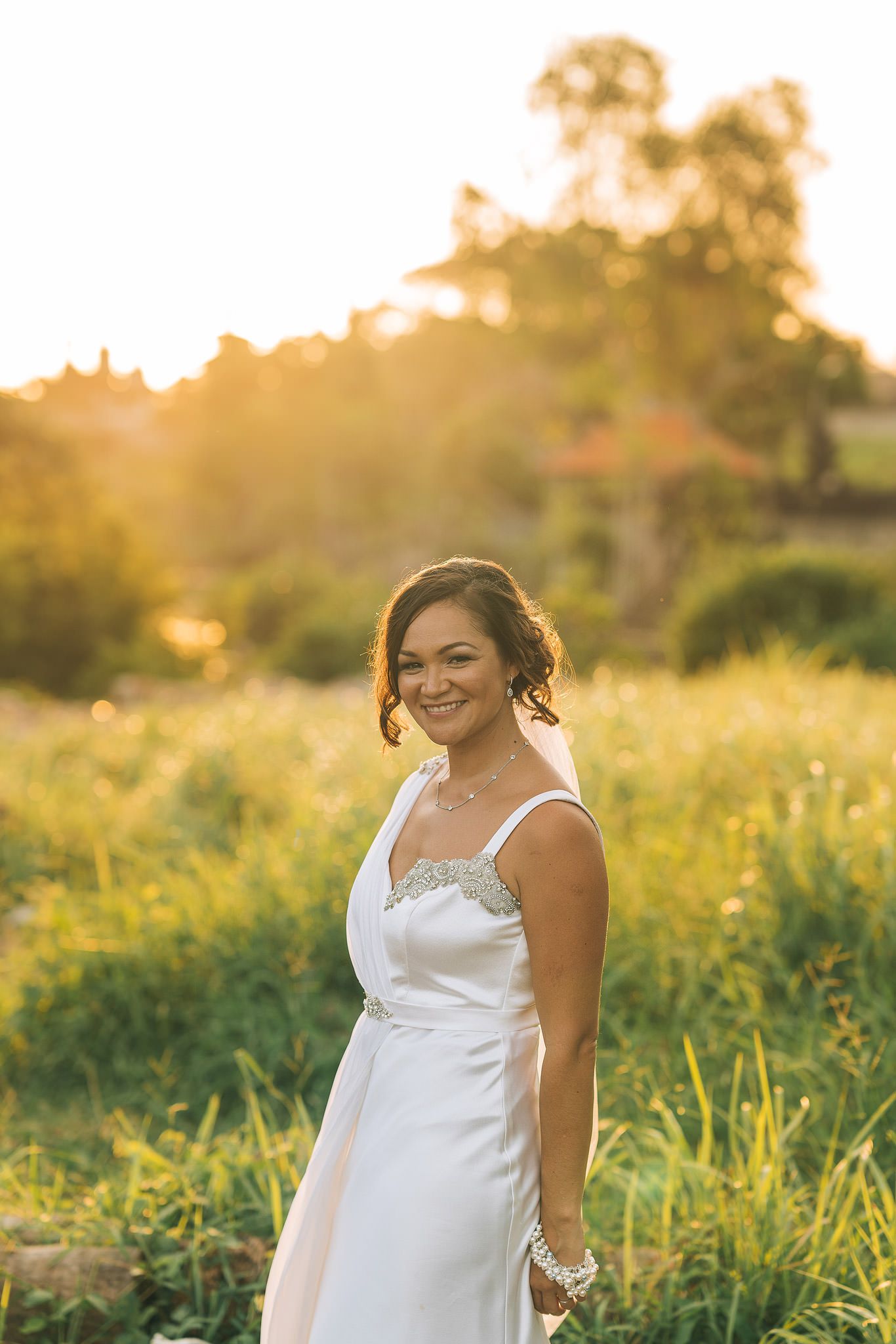 White wedding dress glowing in golden sunset light among tall grass.