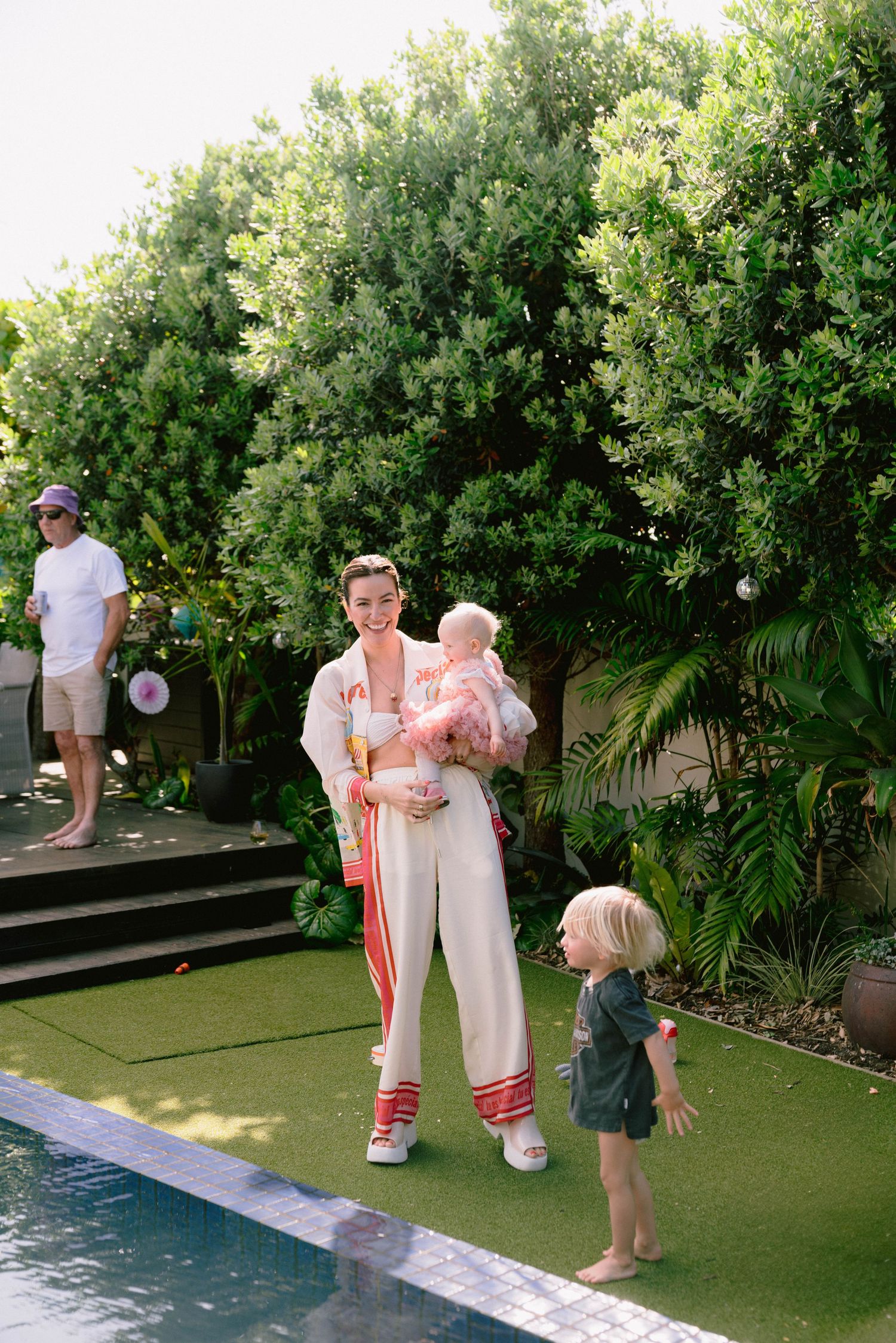 A poolside gathering on artificial turf with lush greenery and palm trees in the background.