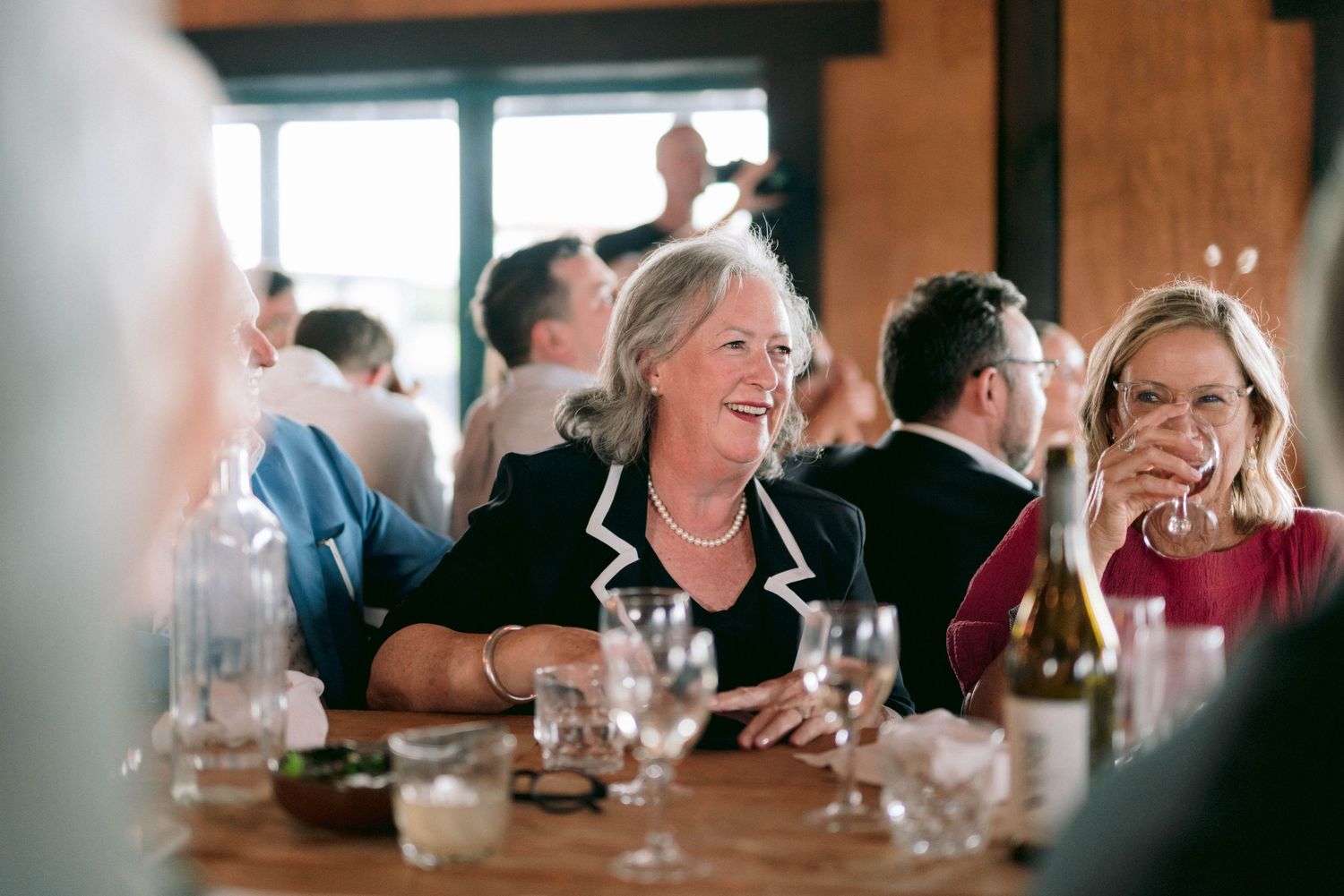 Wedding reception guests enjoying drinks and conversation in rustic indoor venue.