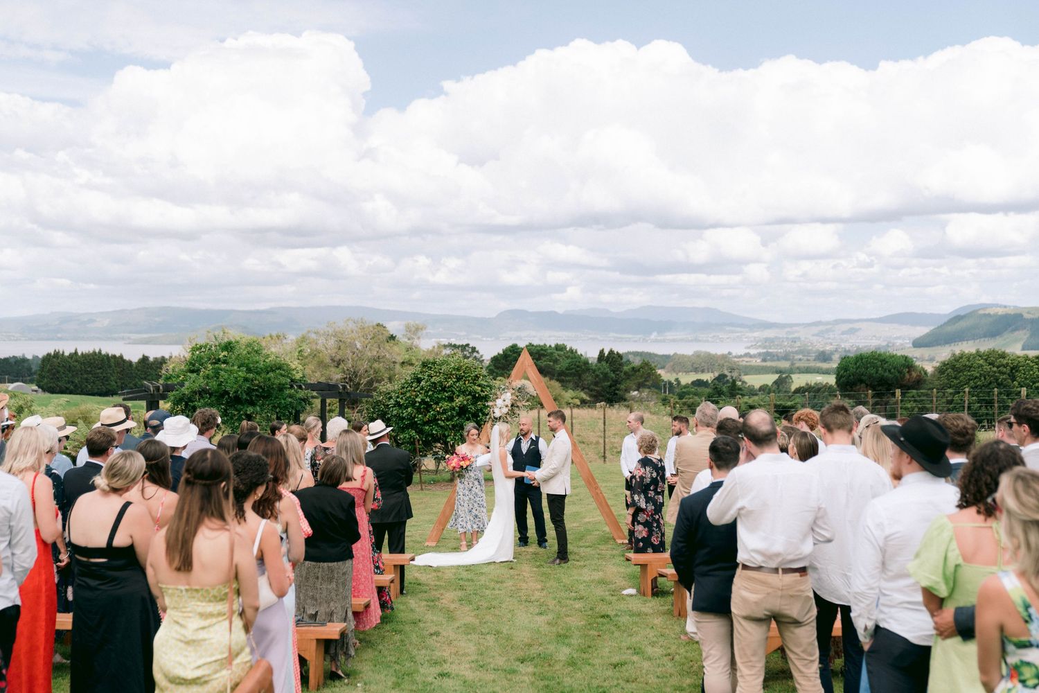 Outdoor wedding ceremony overlooking mountain views with guests seated on lawn chairs.