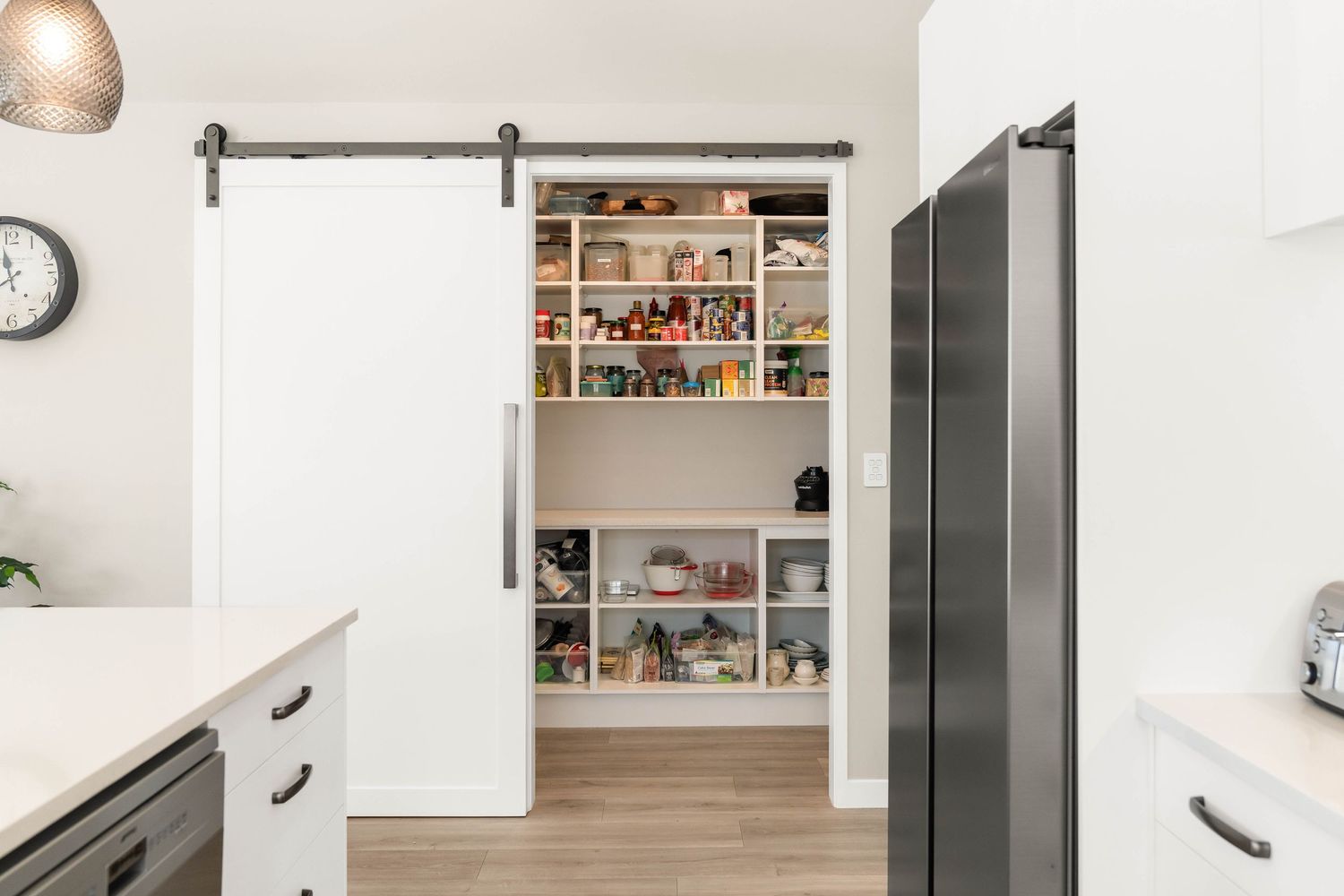Modern white pantry with sliding barn door features organized shelving displaying food items and kitchen supplies.