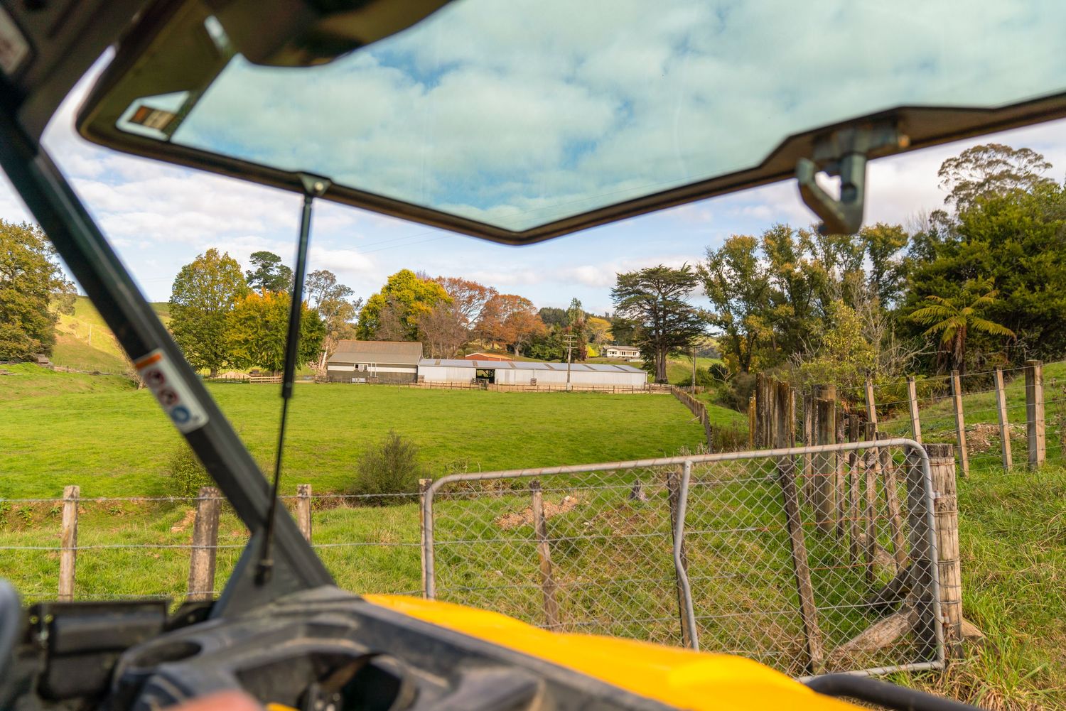 View through utility vehicle windshield of rural farm property with fencing and buildings.
