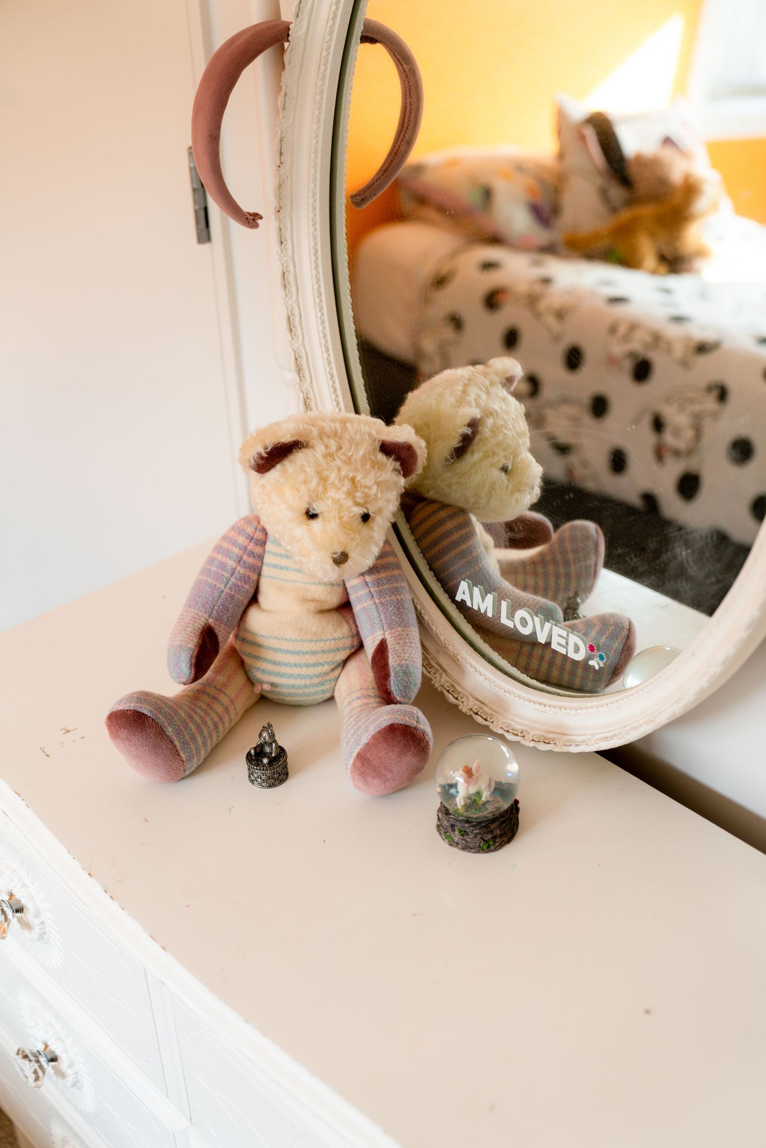 A plush teddy bear in striped clothing sits beside a mirror on a white surface with decorative stones nearby.