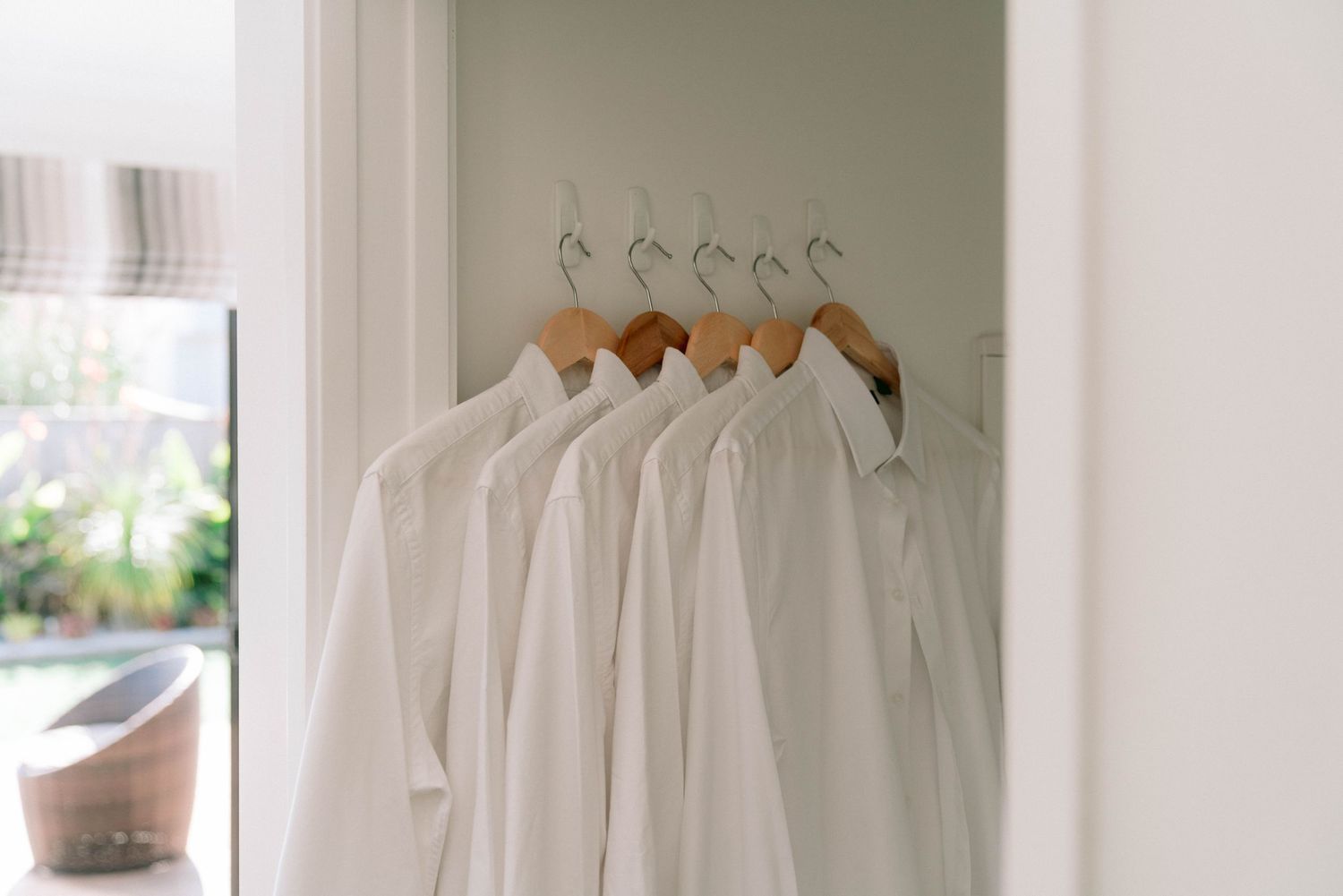 A clean, minimalist closet organization system with white hangers and light wooden shelving against a neutral wall.