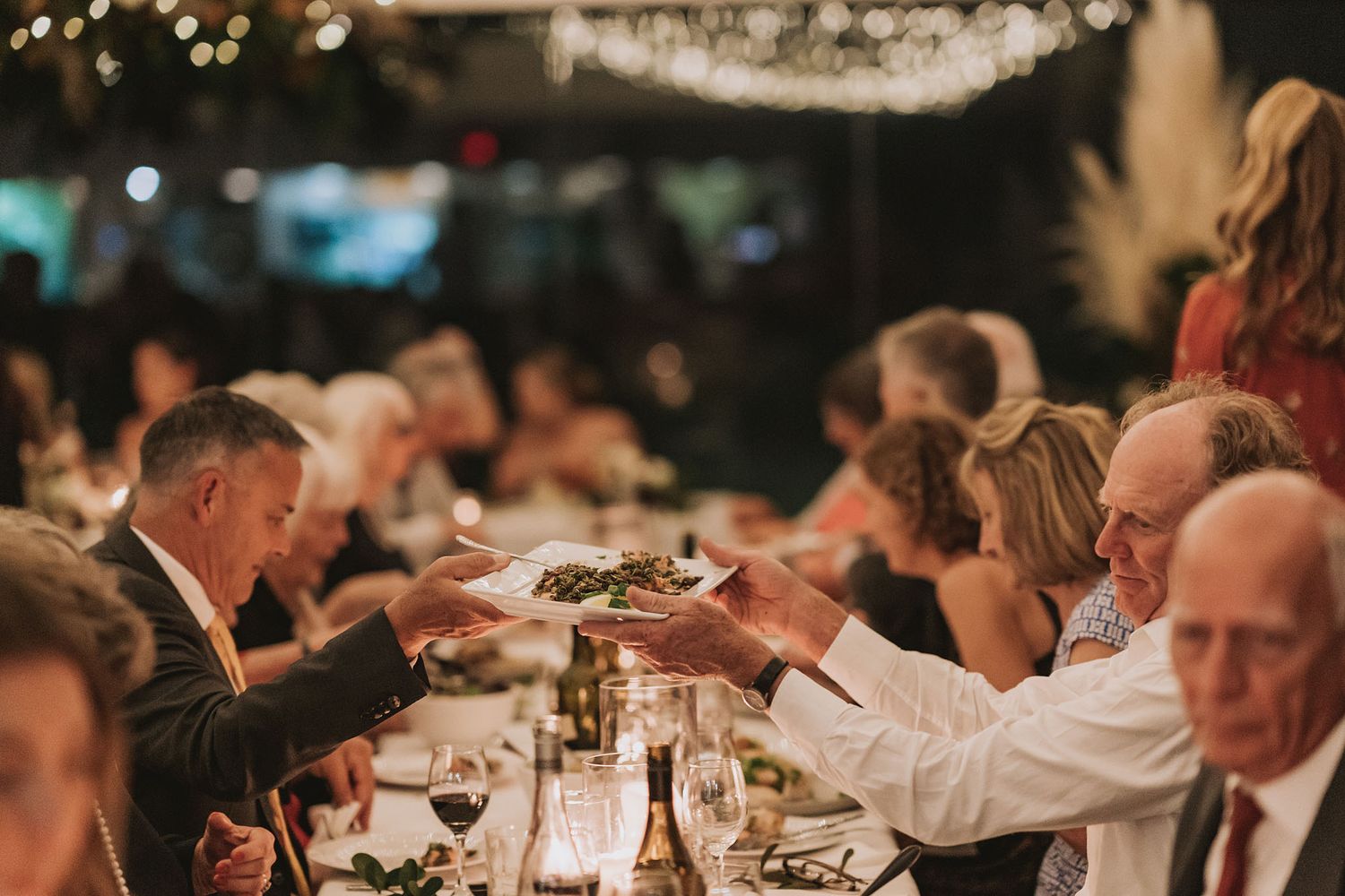 Guests enjoy an elegant wedding reception dinner in a dimly lit banquet hall with soft bokeh lighting and table settings.