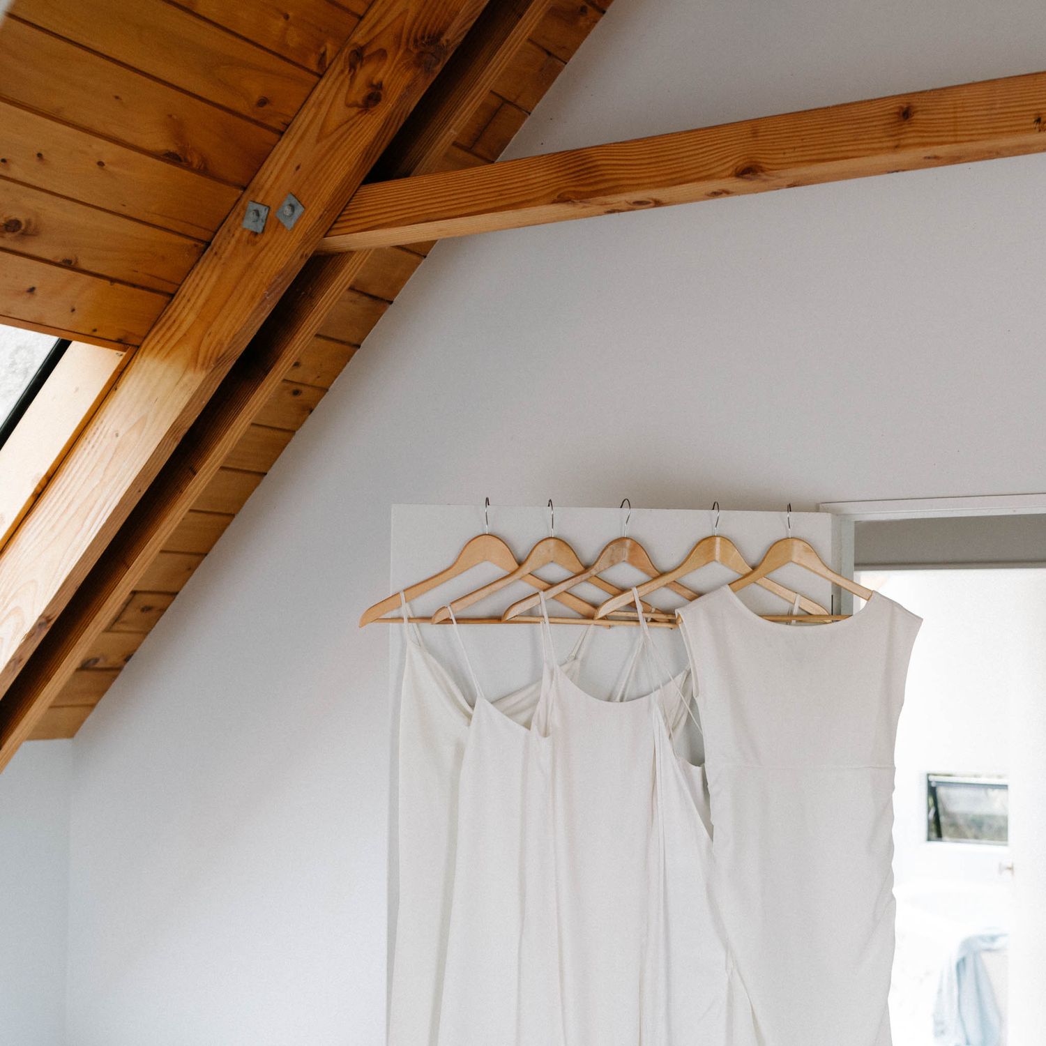 Empty white metal hangers neatly spaced on a minimalist closet rod under a slanted wooden ceiling.