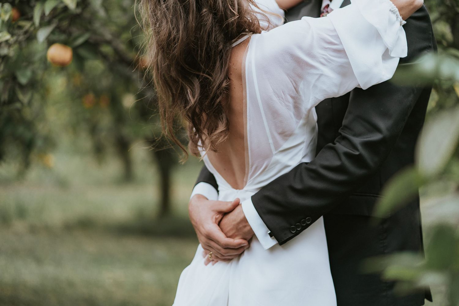 Close up of newlywed couple embracing in white wedding dress and black suit during outdoor garden ceremony.
