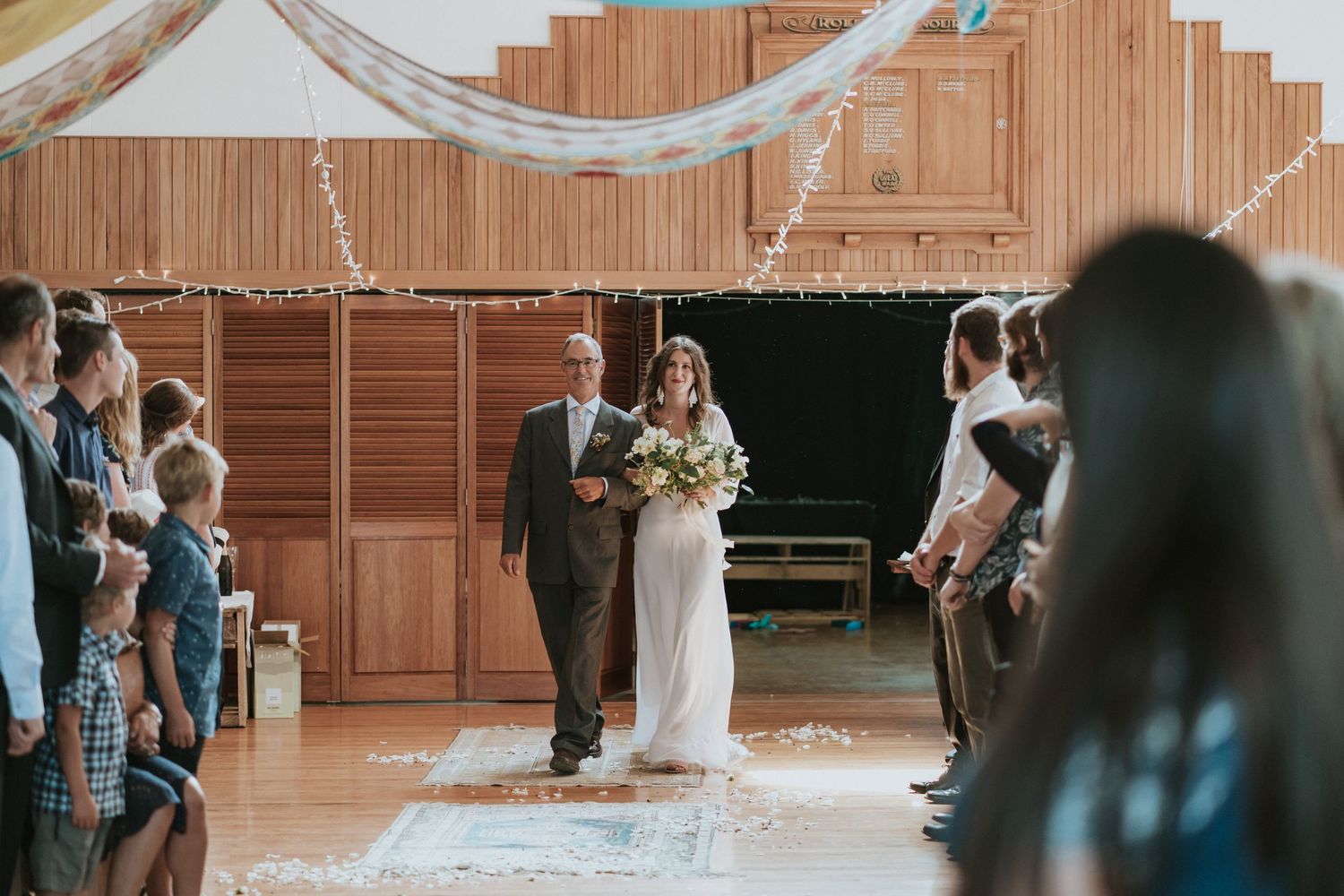 String lights and white fabric decorations hang elegantly across a wooden barn ceiling during a wedding celebration.