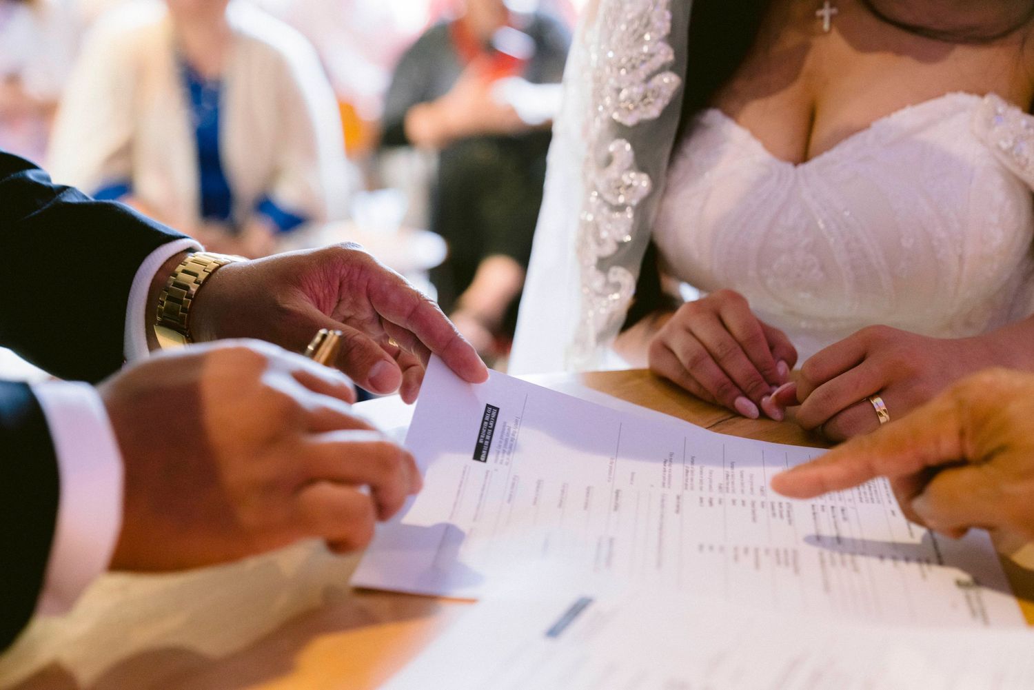 A bride and groom signing wedding documents while sitting at a table during their ceremony.