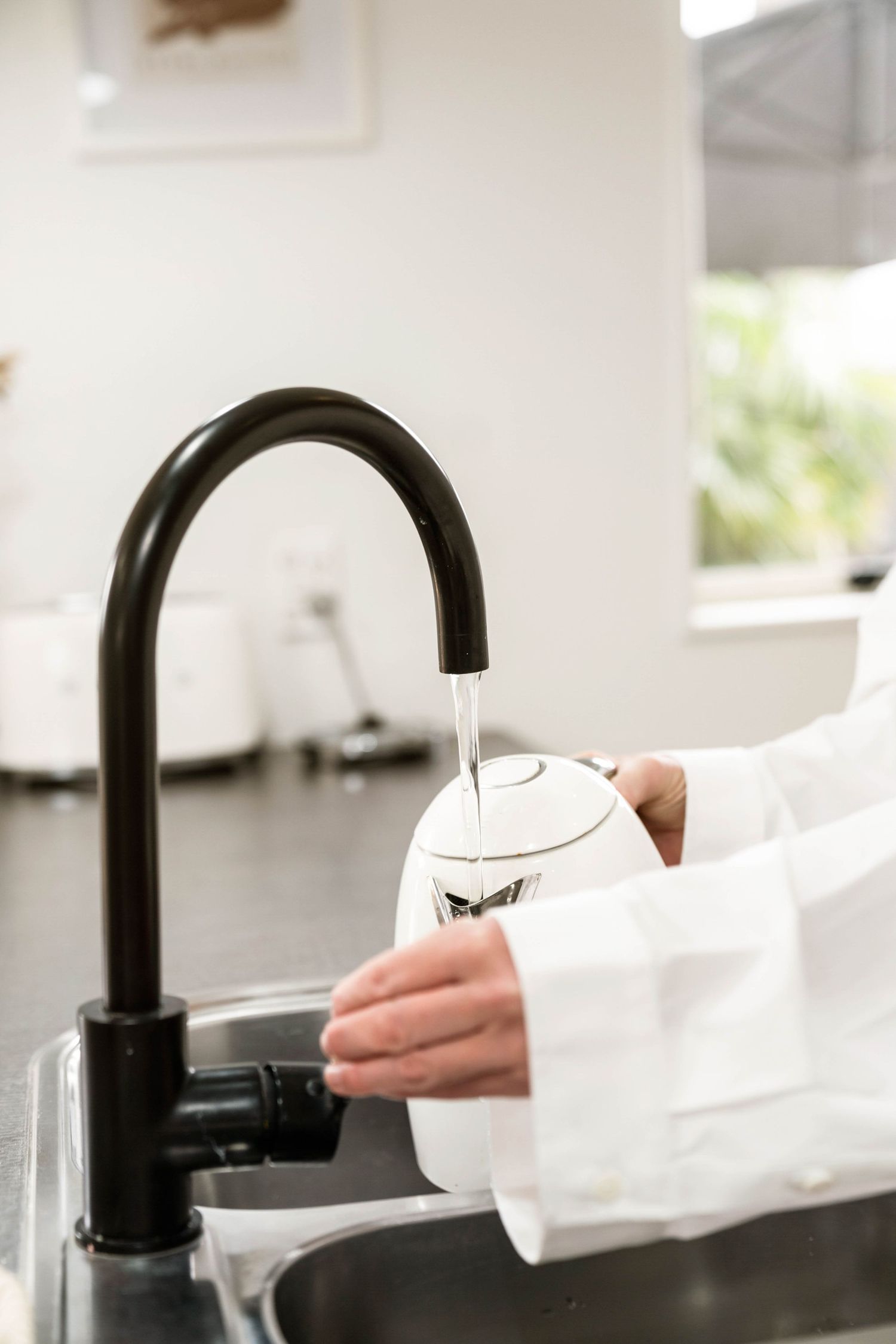 Person filling a white cup from a modern black faucet in a sleek kitchen.