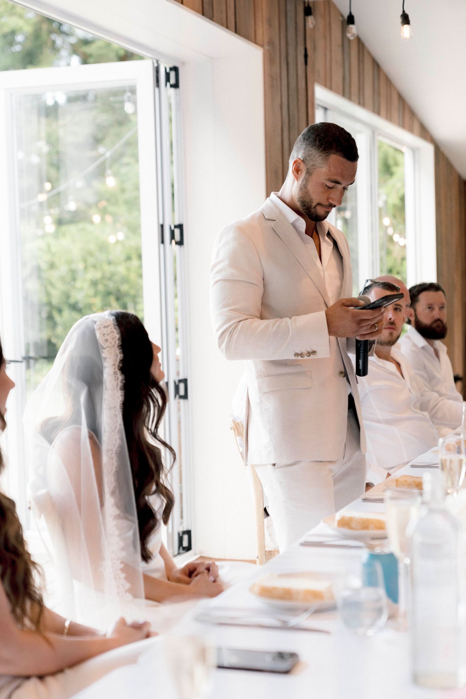 Wedding reception speaker stands at head table giving toast during dinner.