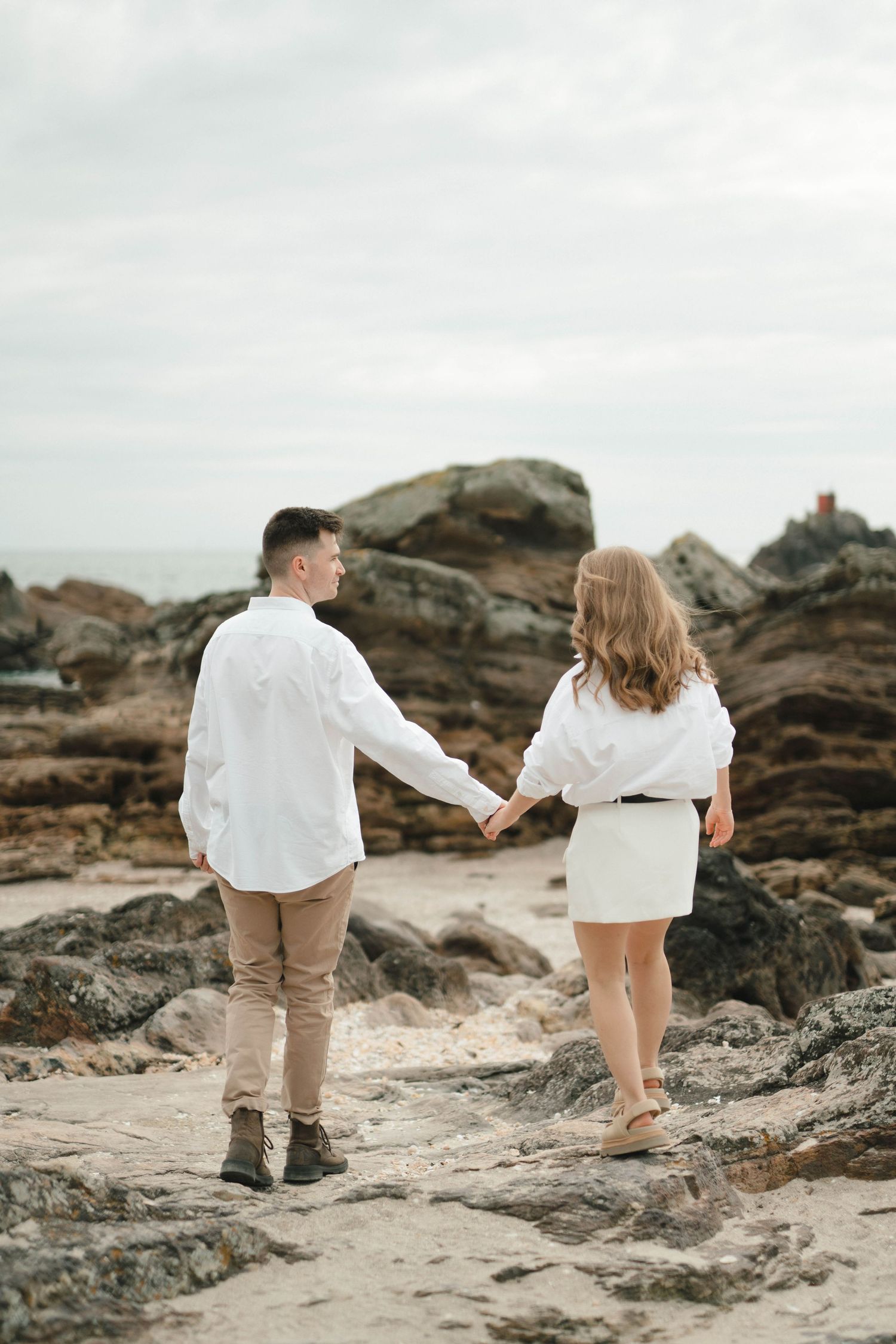 A couple explores rocky coastal terrain wearing matching white shirts and neutral bottoms.