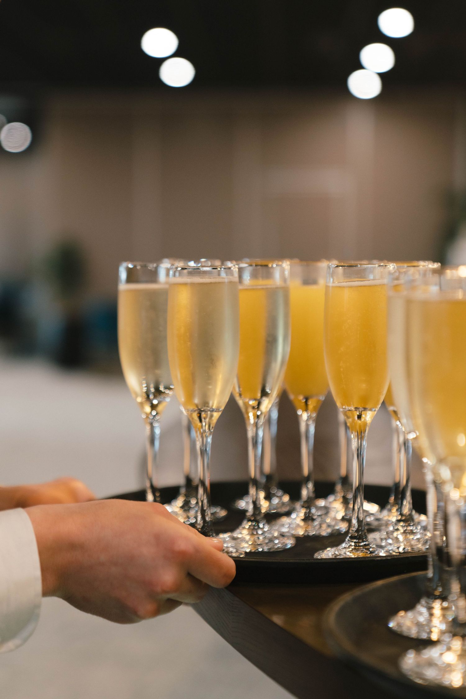 A server holds a tray of champagne flutes filled with golden bubbly drinks at an elegant event.