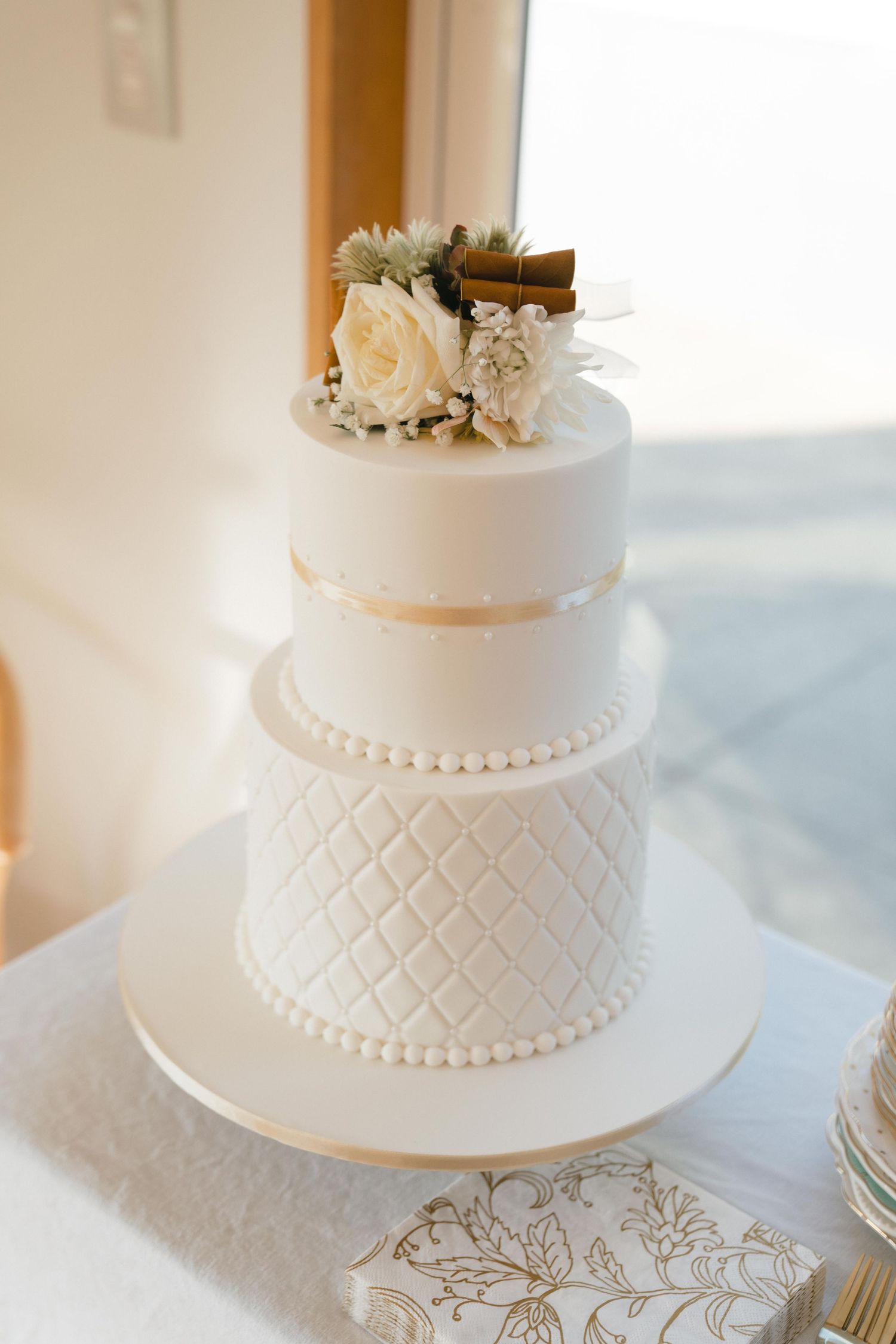 Elegant white wedding cake with quilted pattern, pearl details and fresh peach roses on top.