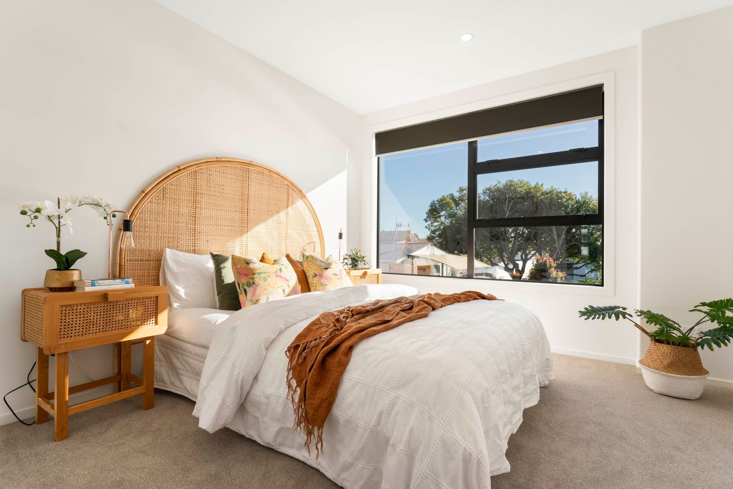 Bright coastal bedroom with rattan headboard, wooden furniture and large window offering natural light.