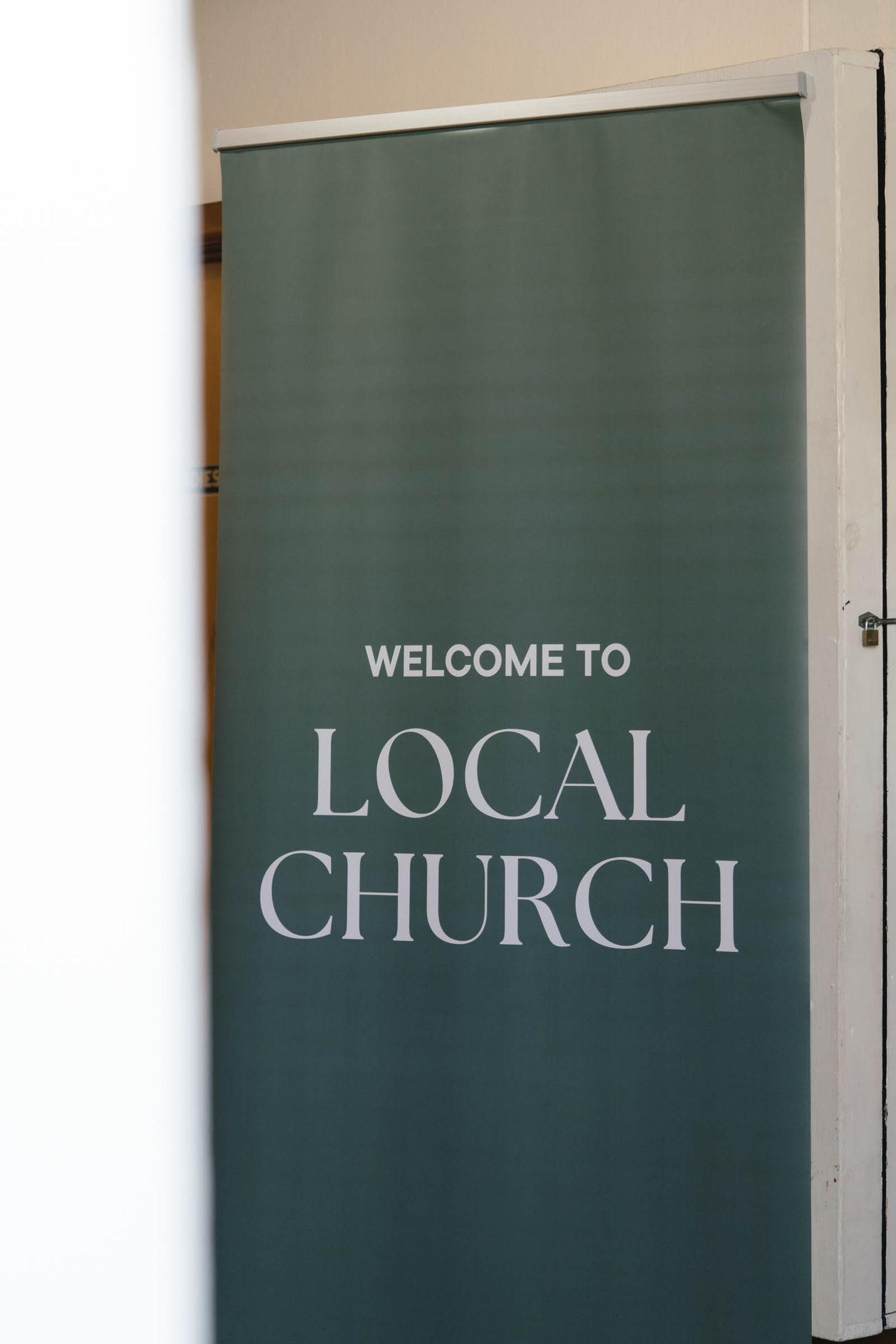 A green door sign reading 'WELCOME TO LOCAL CHURCH' mounted on a white wall.