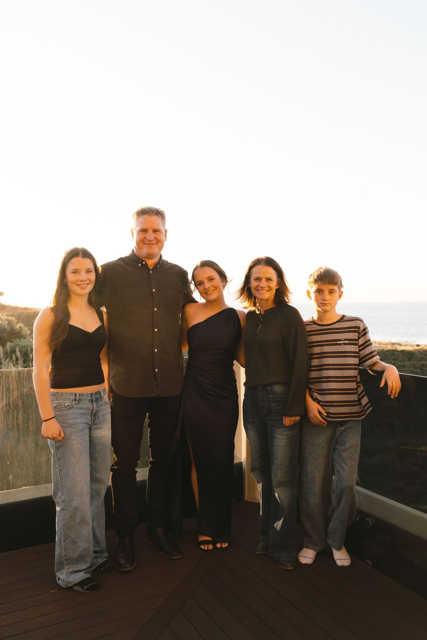 Family group photo on rooftop deck with casual and formal mixed attire at sunset.