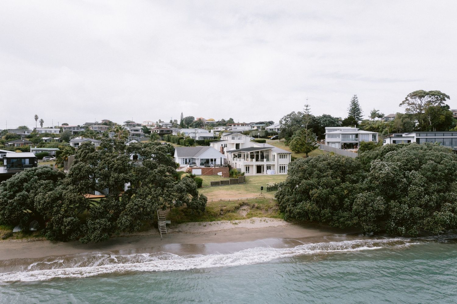 Beachfront homes and properties nestled among trees along a coastal shoreline in New Zealand.