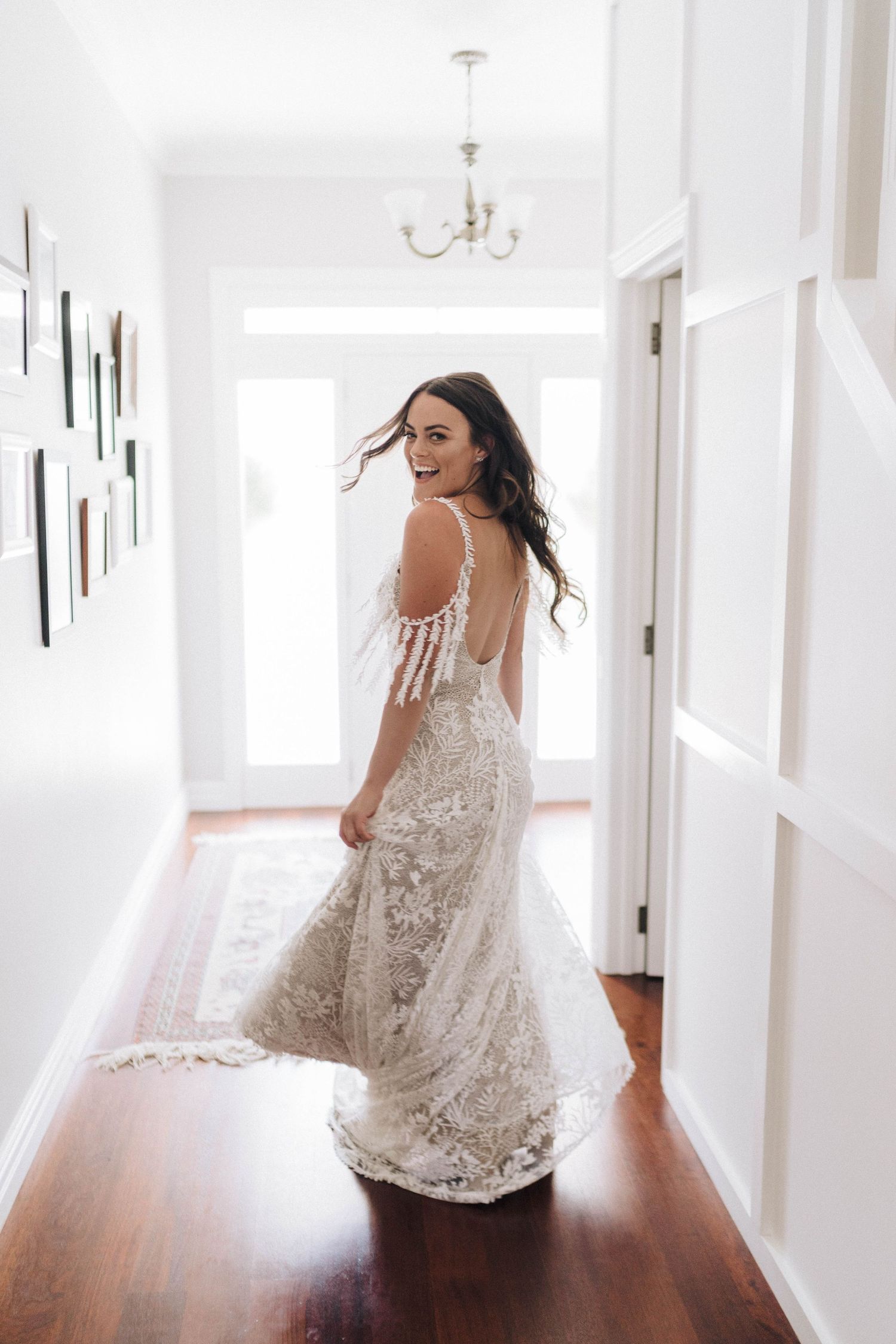 Person in a flowing lace dress twirls joyfully in a sunlit hallway.